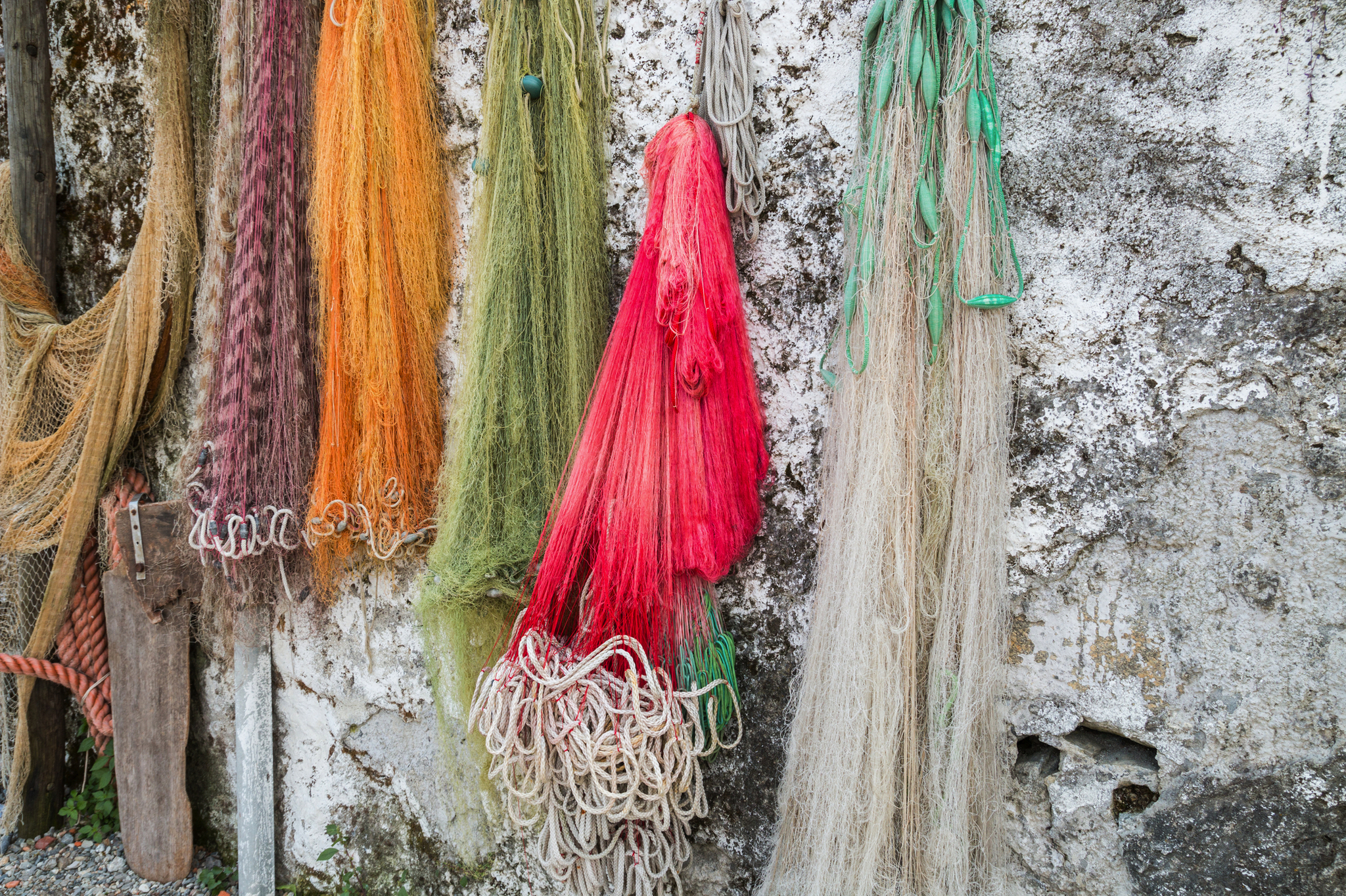 Bunte Fischernetze hängen an einer alten Mauer.