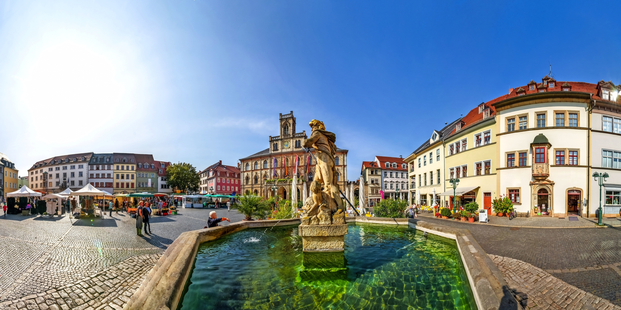 Marktplatz mit Brunnen und historischen Gebäuden bei Sonnenlicht.