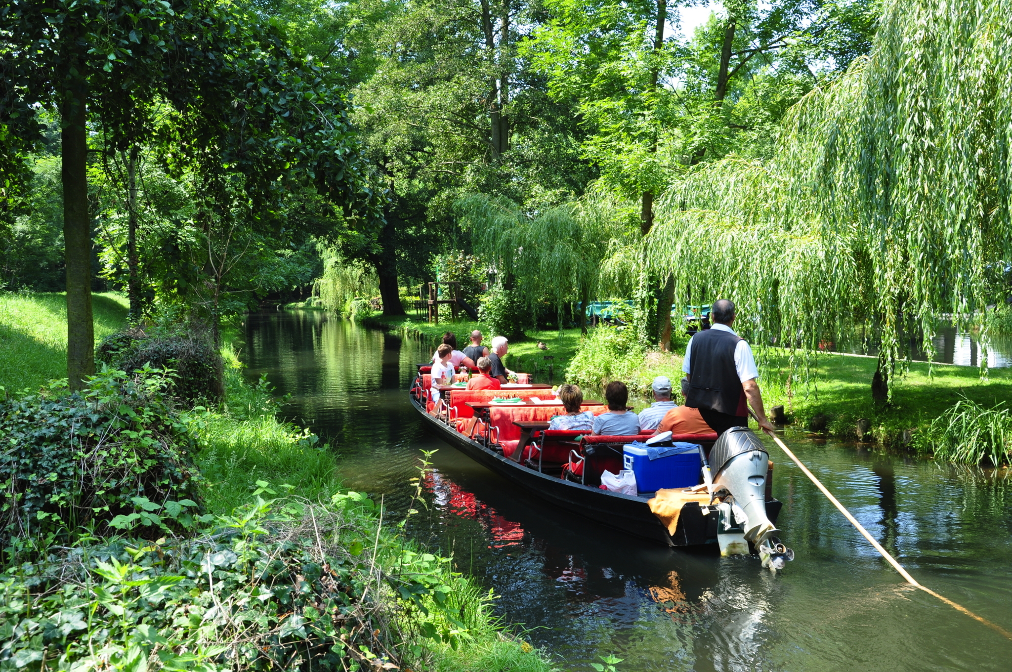 Menschen auf einem Boot im grünen Kanal, von Bäumen umgeben.