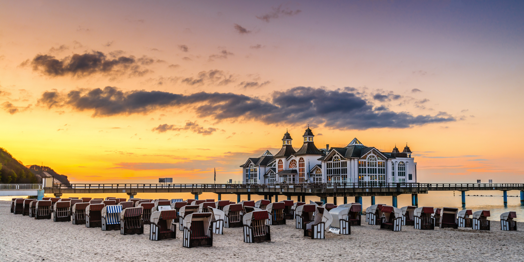 Seebrücke bei Sonnenuntergang mit Strandkörben im Vordergrund.