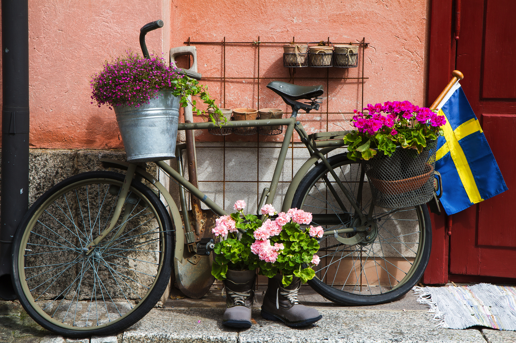 Fahrrad mit Blumenkörben, schwedische Flagge neben rotem Haus.