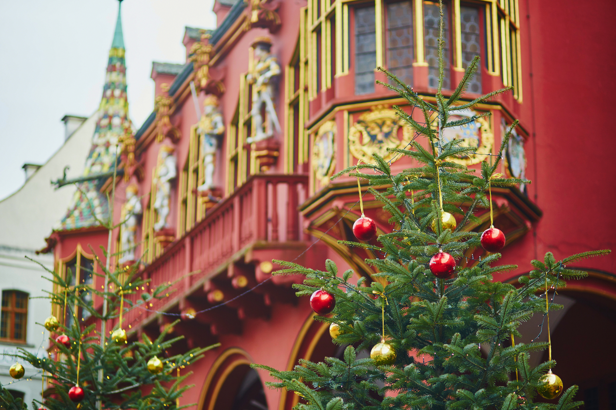 Zwei Weihnachtsbäume vor einem roten, verzierten Gebäude.