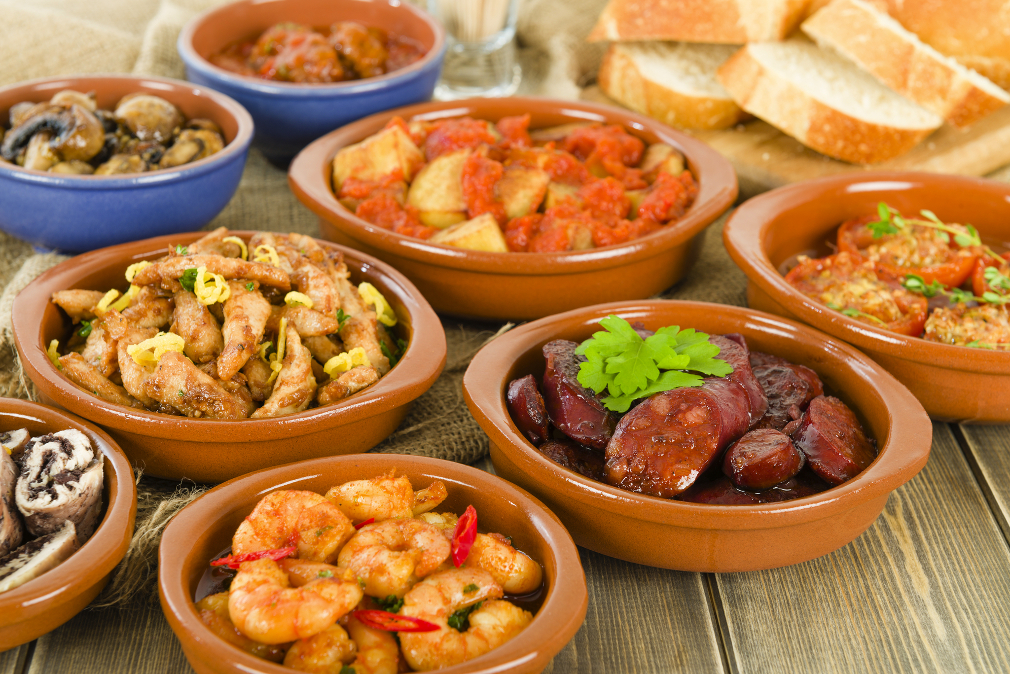 Verschiedene Tapas-Gerichte in Schüsseln auf Holztisch.