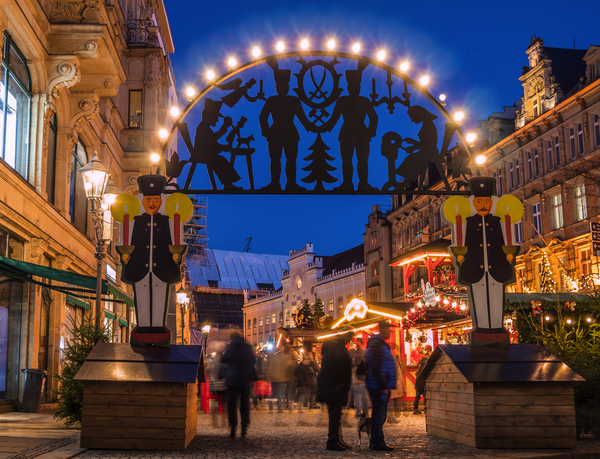 Eingang eines Weihnachtsmarktes mit beleuchtetem Schwibbogen und Menschen.