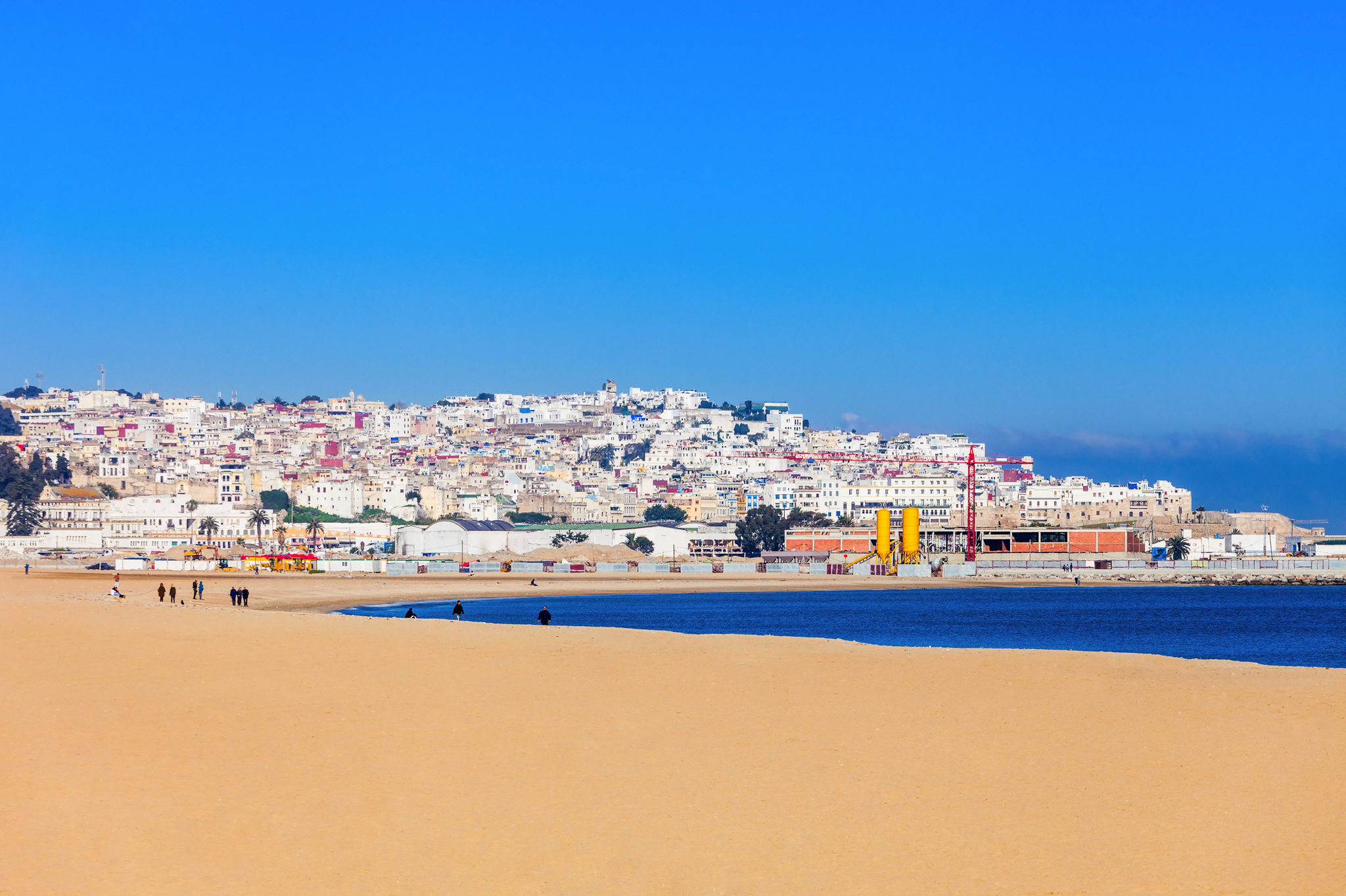 Stadtansicht von Tanger mit Sandstrand im Vordergrund unter blauem Himmel.