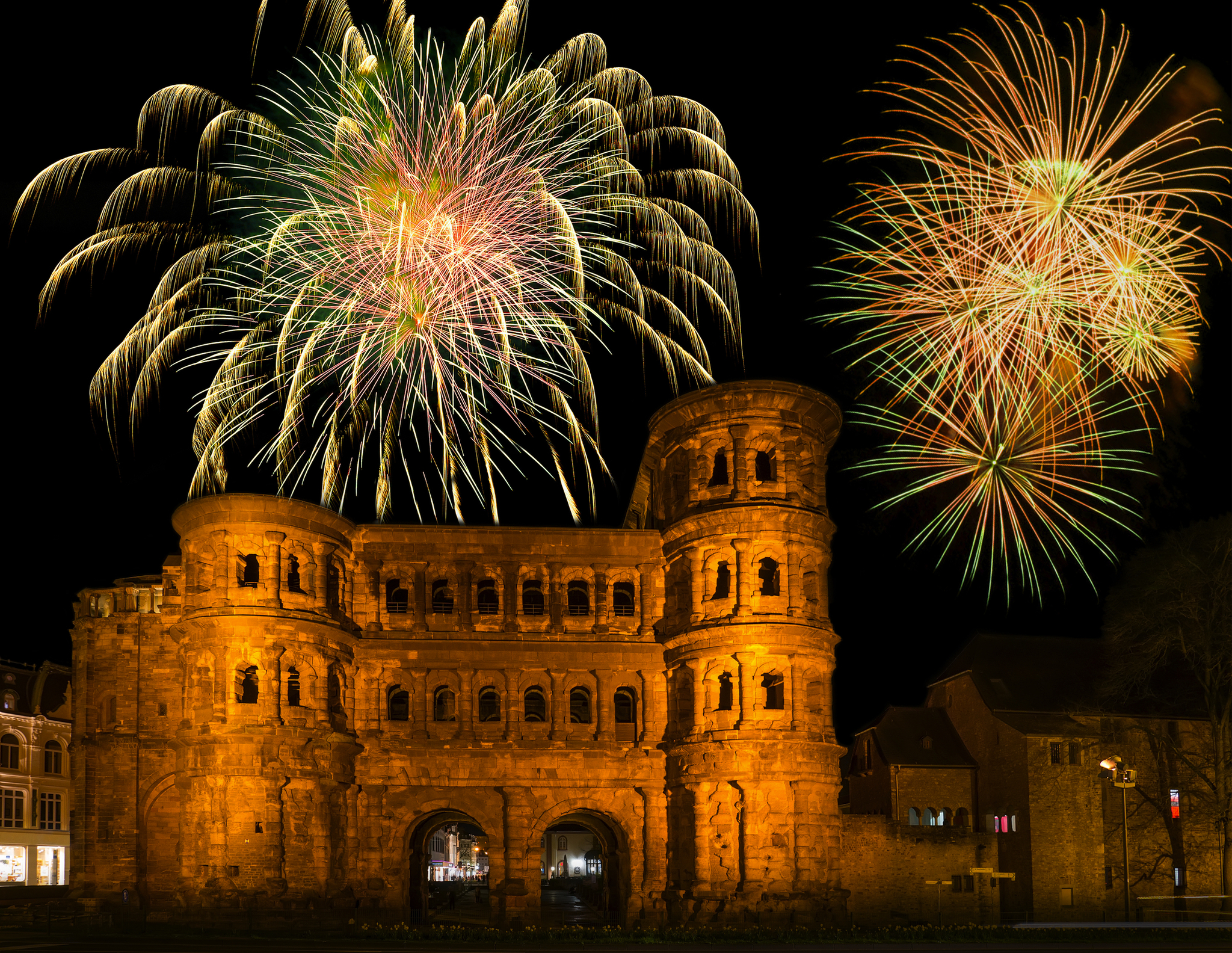 Alte römische Stadttor-Ruine bei Nacht mit Feuerwerk im Hintergrund.