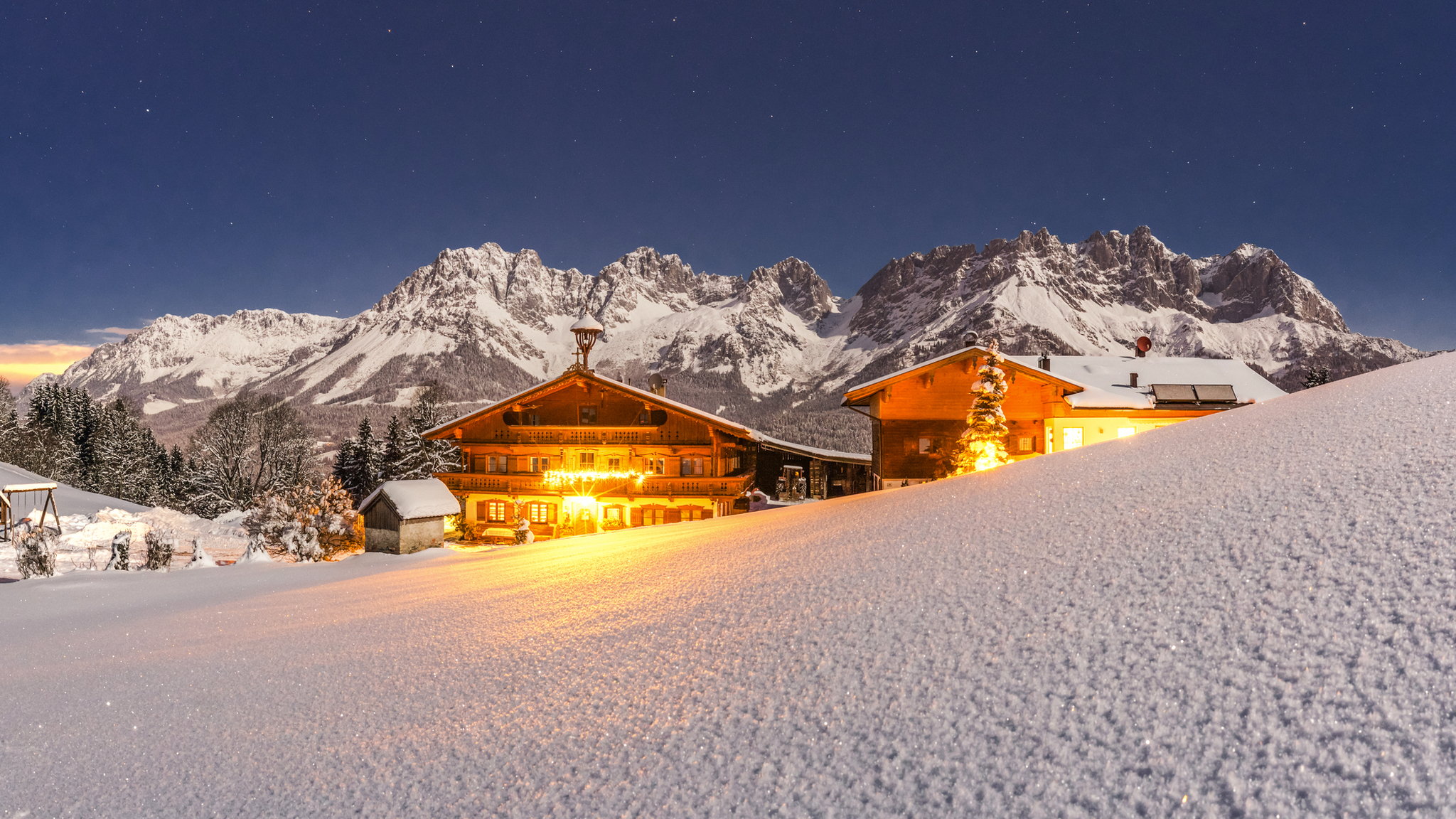 Schneebedeckte Berghütten vor einer Bergkulisse bei Nacht.