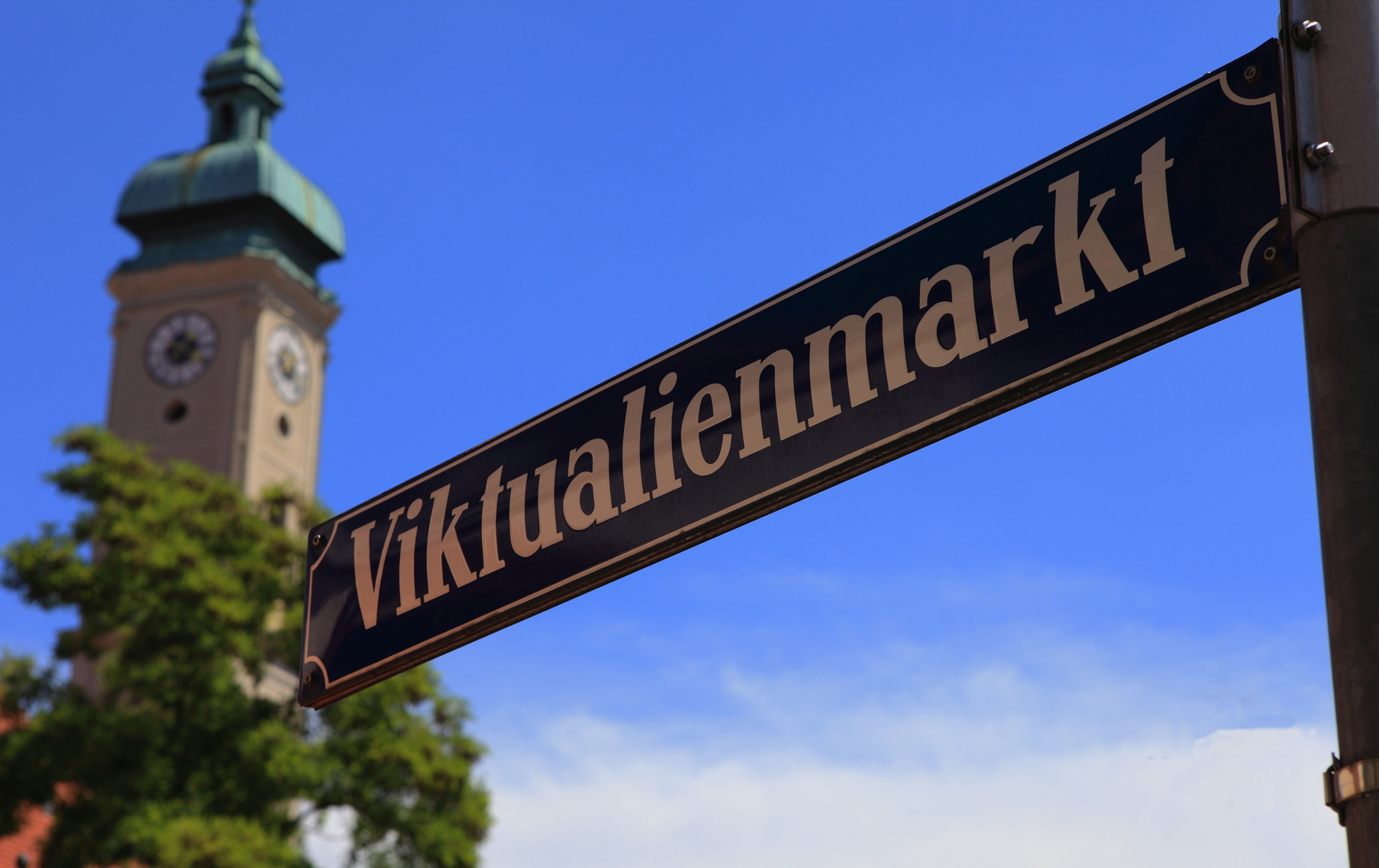 Straßenschild mit der Aufschrift Viktualienmarkt vor einem Kirchturm.