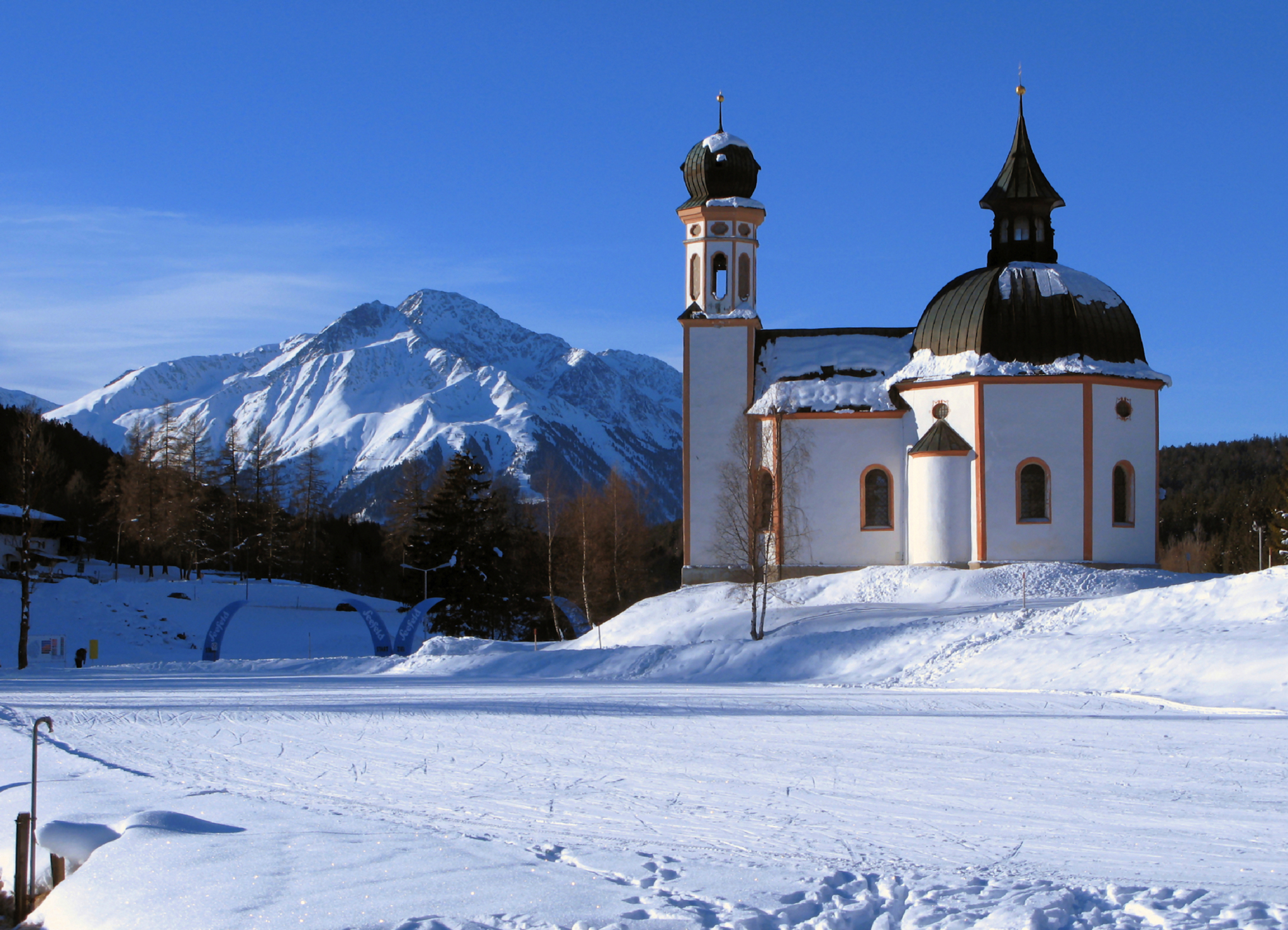 Kirche in verschneiter Alpenlandschaft mit Bergen im Hintergrund.