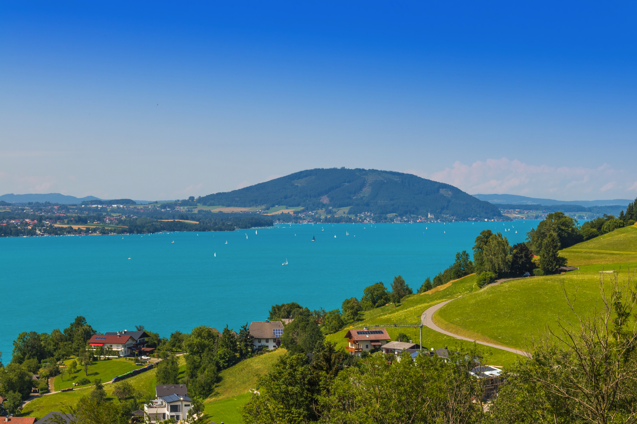 Blick auf See mit Segelbooten, grüne Hügel und Berg im Hintergrund.