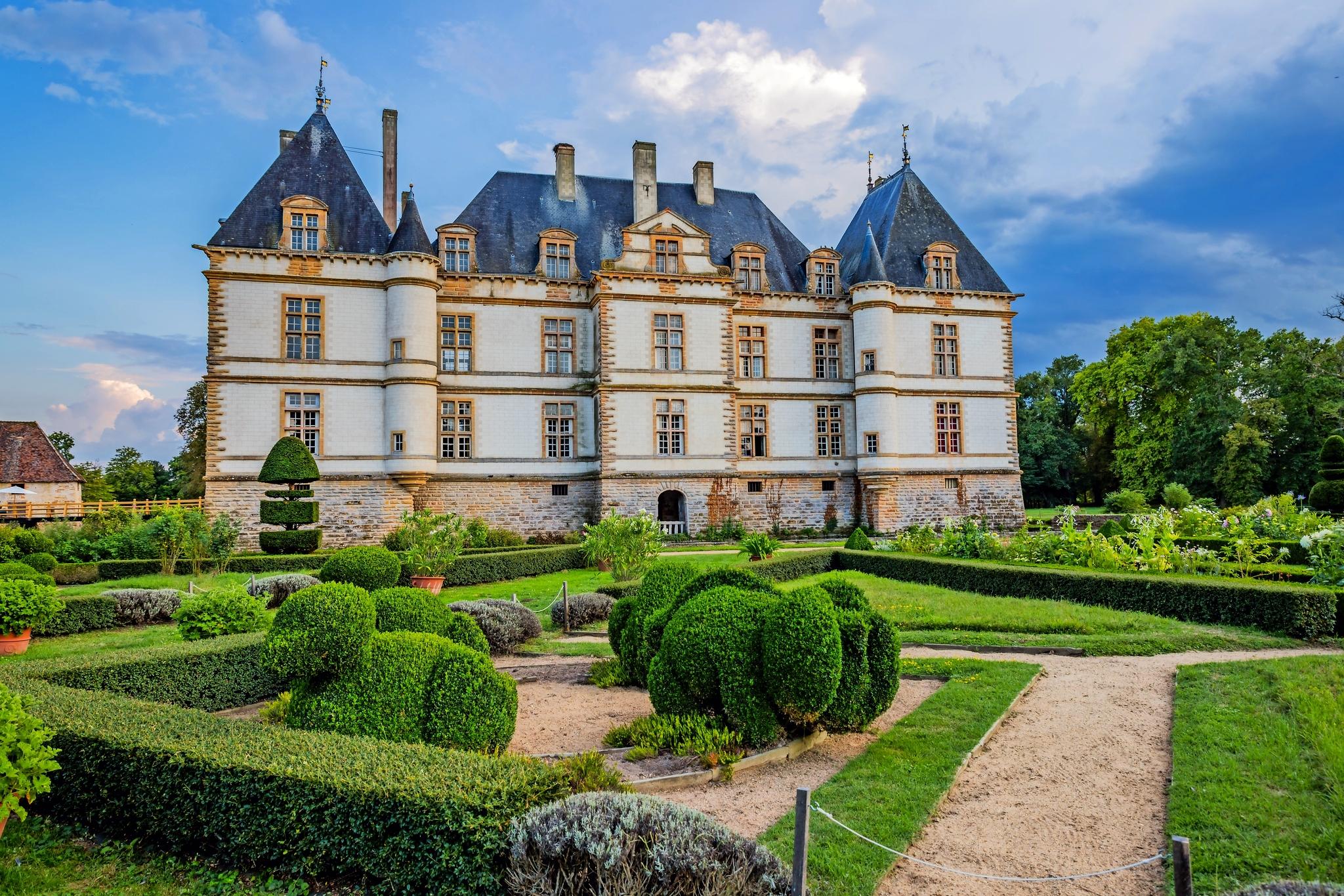 Schloss mit gepflegtem Garten bei bewölktem Himmel.
