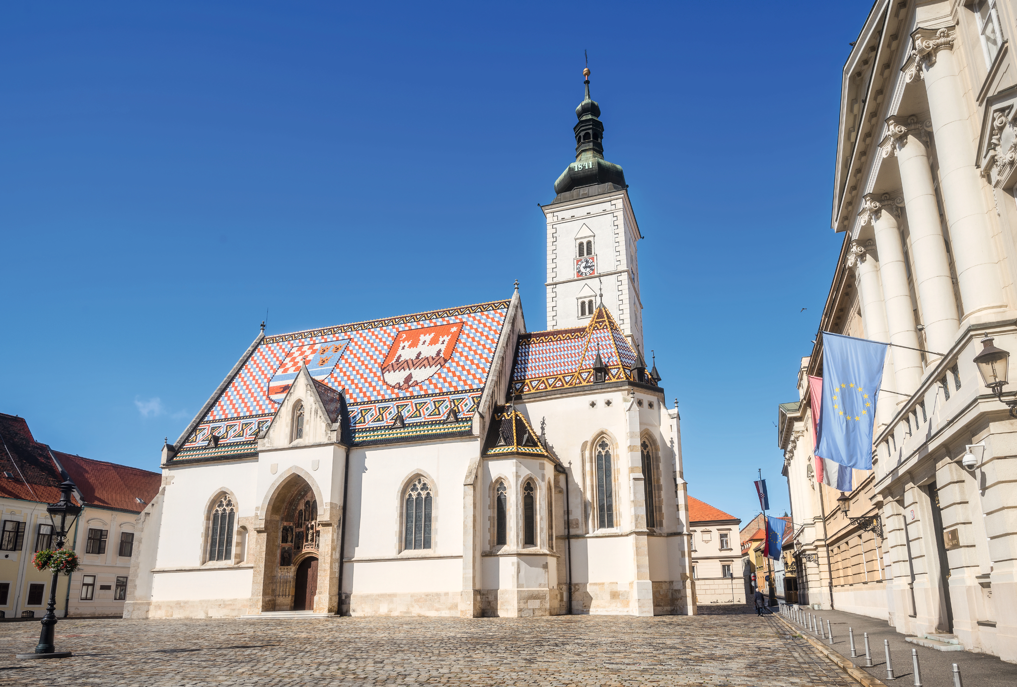 Kirche mit buntem Dach und Glockenturm auf einem gepflasterten Platz.