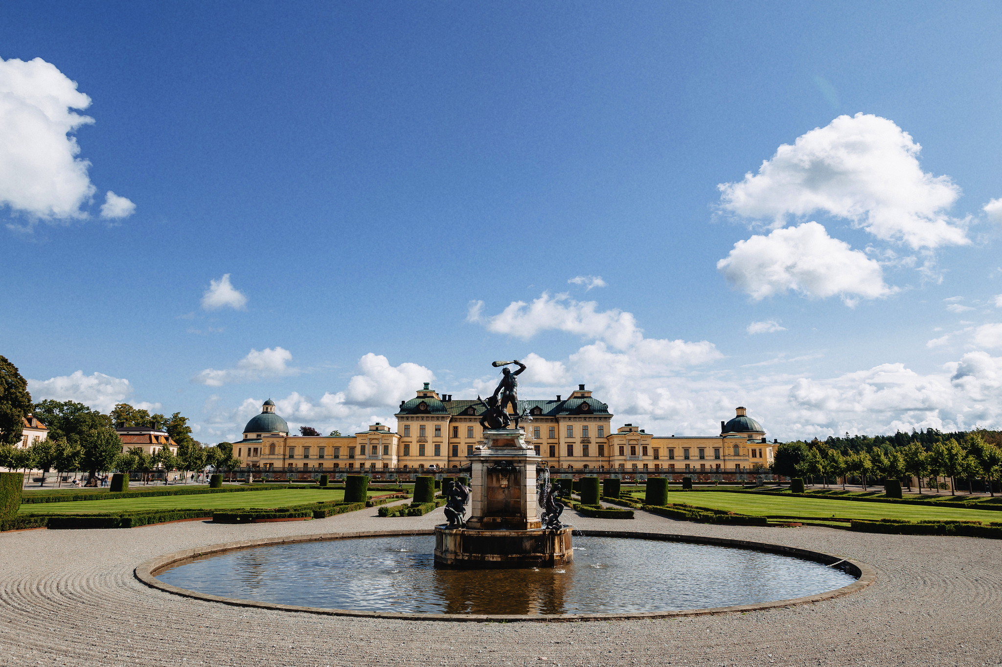 Barockes Schloss mit Springbrunnen und Gärten bei blauem Himmel.