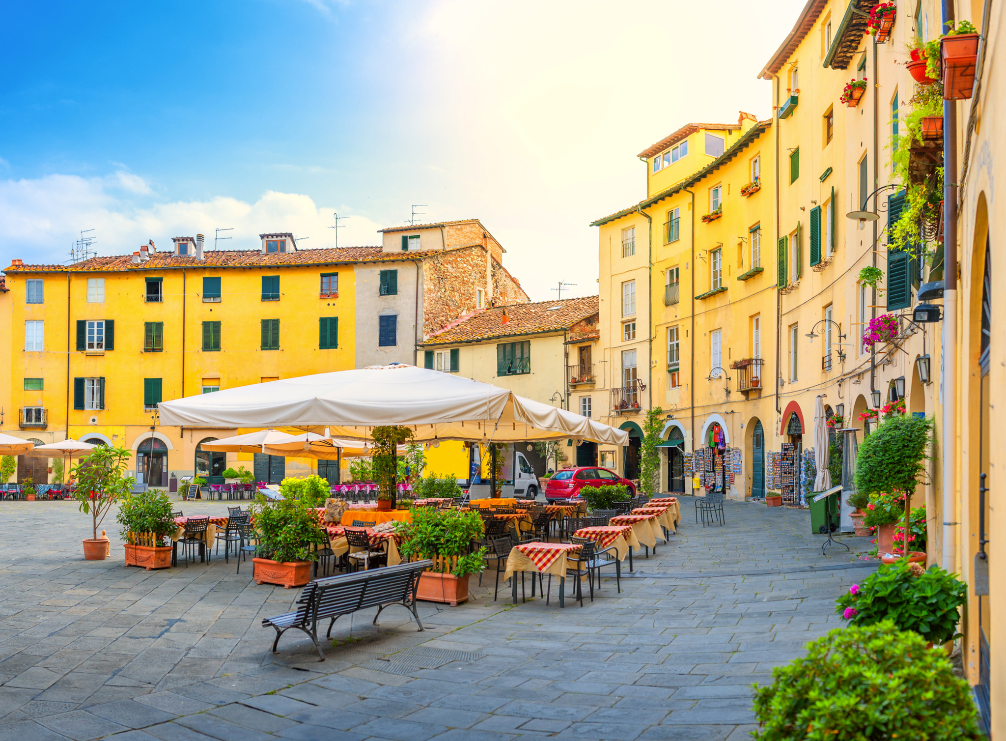 Piazza dell' Anfiteatro in Lucca, Italien Italienischer Platz mit Cafés und gelben Gebäuden bei sonnigem Wetter.