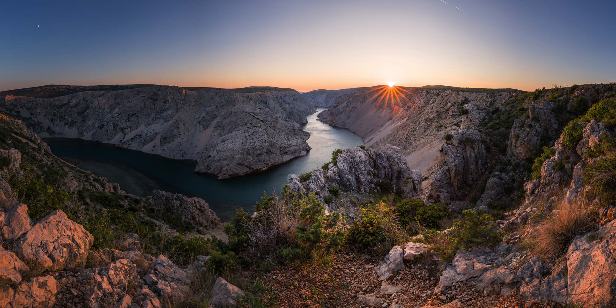 Sonnenuntergang über einer Flussklamm mit felsigen Ufern.