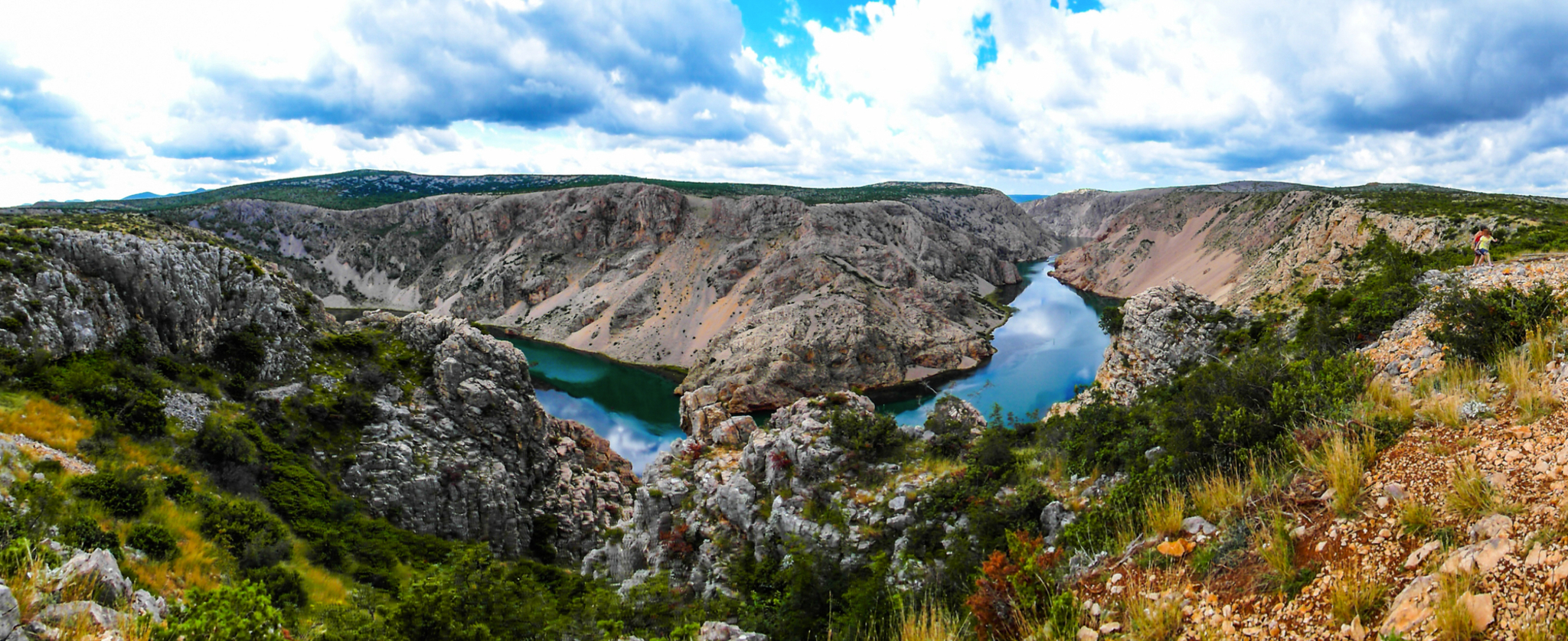 Panoramablick auf eine Flusslandschaft in einer felsigen Schlucht unter bewölktem Himmel.