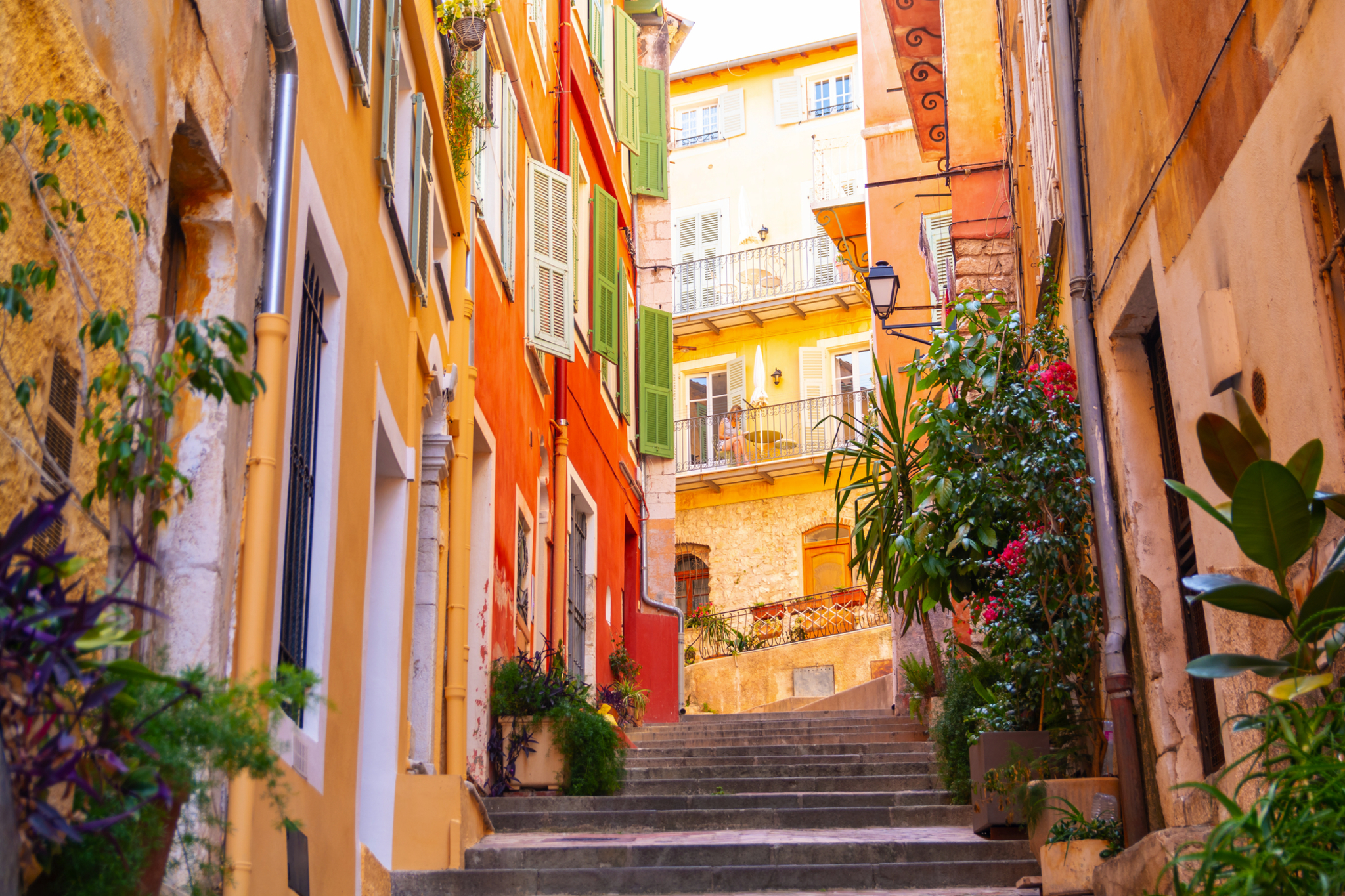 Bunte Häuser an enger, steiler Gasse mit Treppen und Pflanzen.
