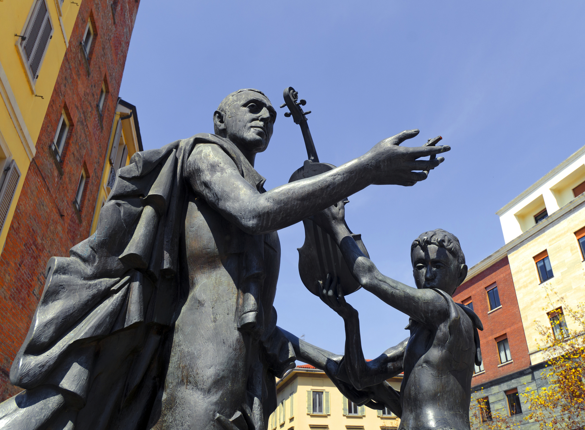 Bronzestatue eines Mannes und eines Kindes mit Geige vor Gebäuden.