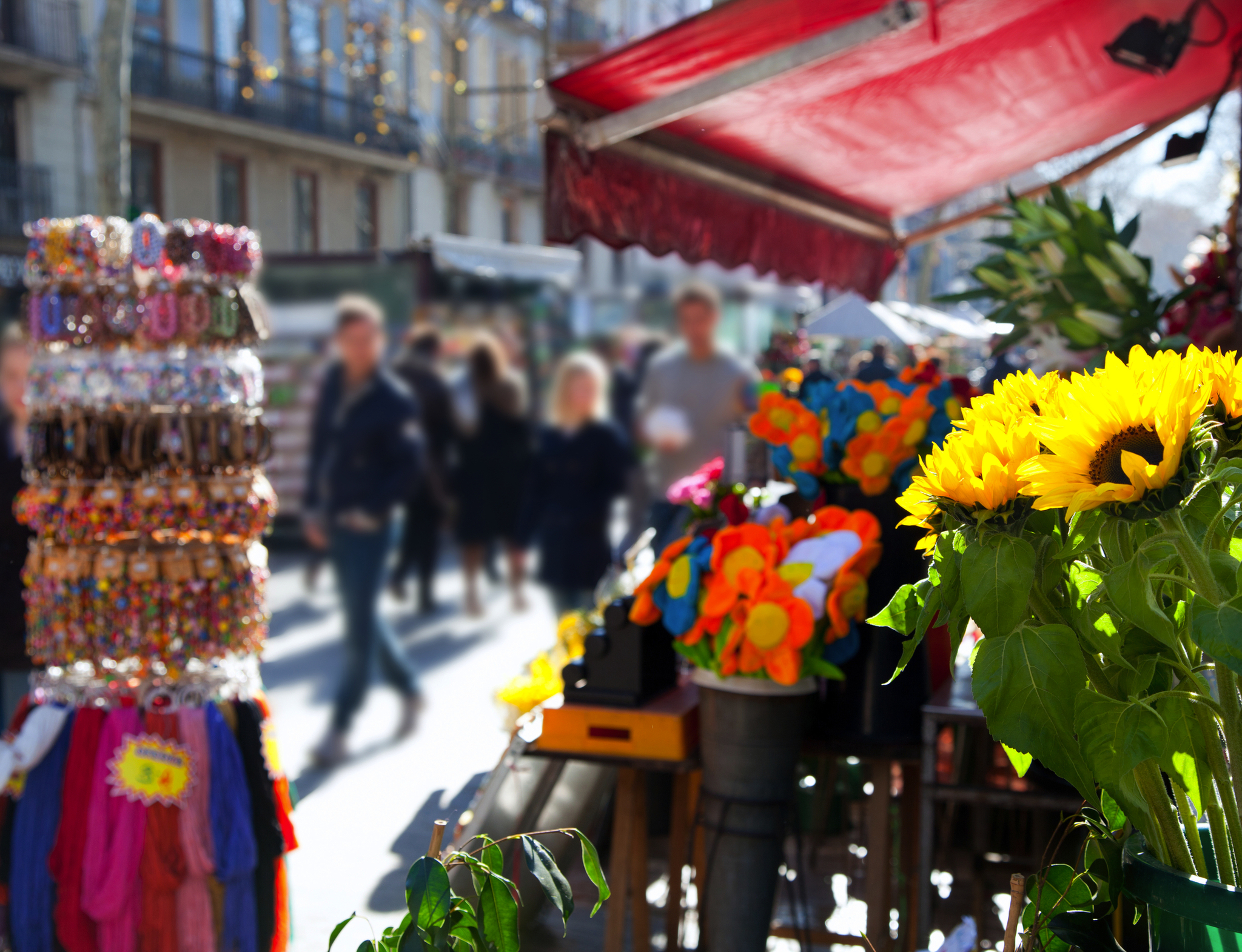 Marktstand mit Blumen und Schmuck, unscharfe Passanten im Hintergrund.