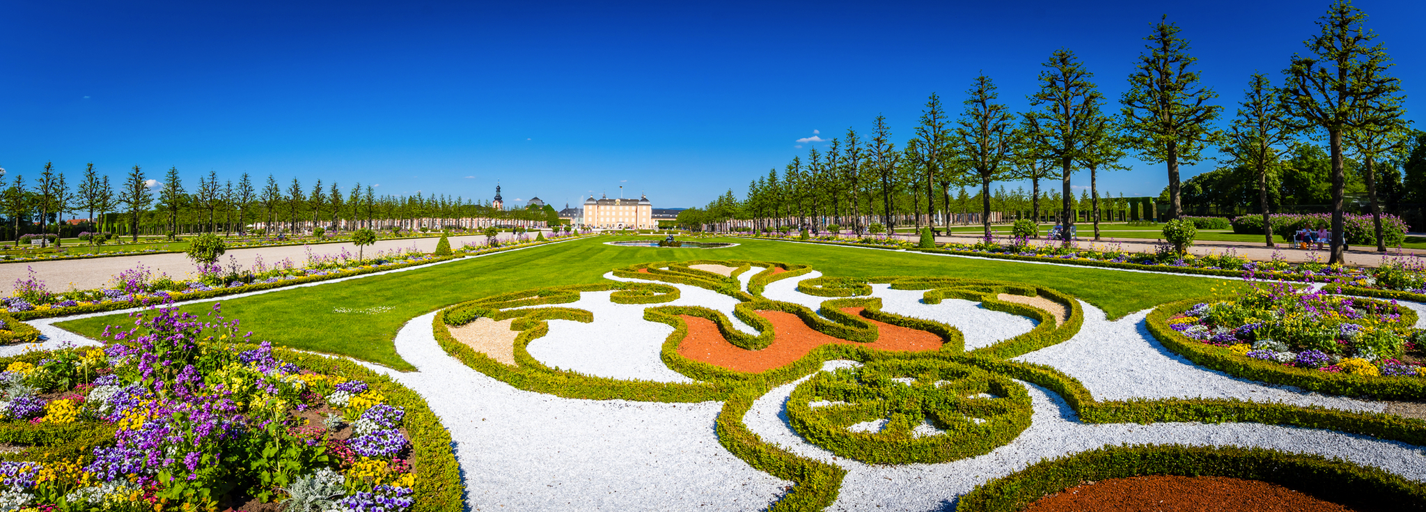 Ein symmetrischer Schlossgarten mit kunstvollen Beeten und blühenden Pflanzen.