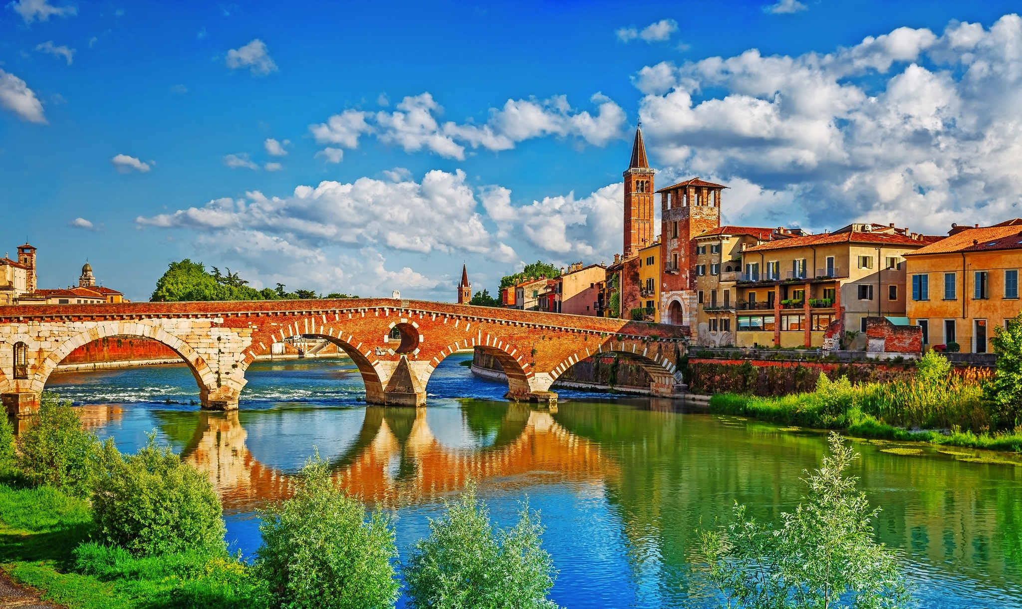 Historische Brücke über Fluss in malerischer Stadt mit Kirchturm und bunten Häusern.