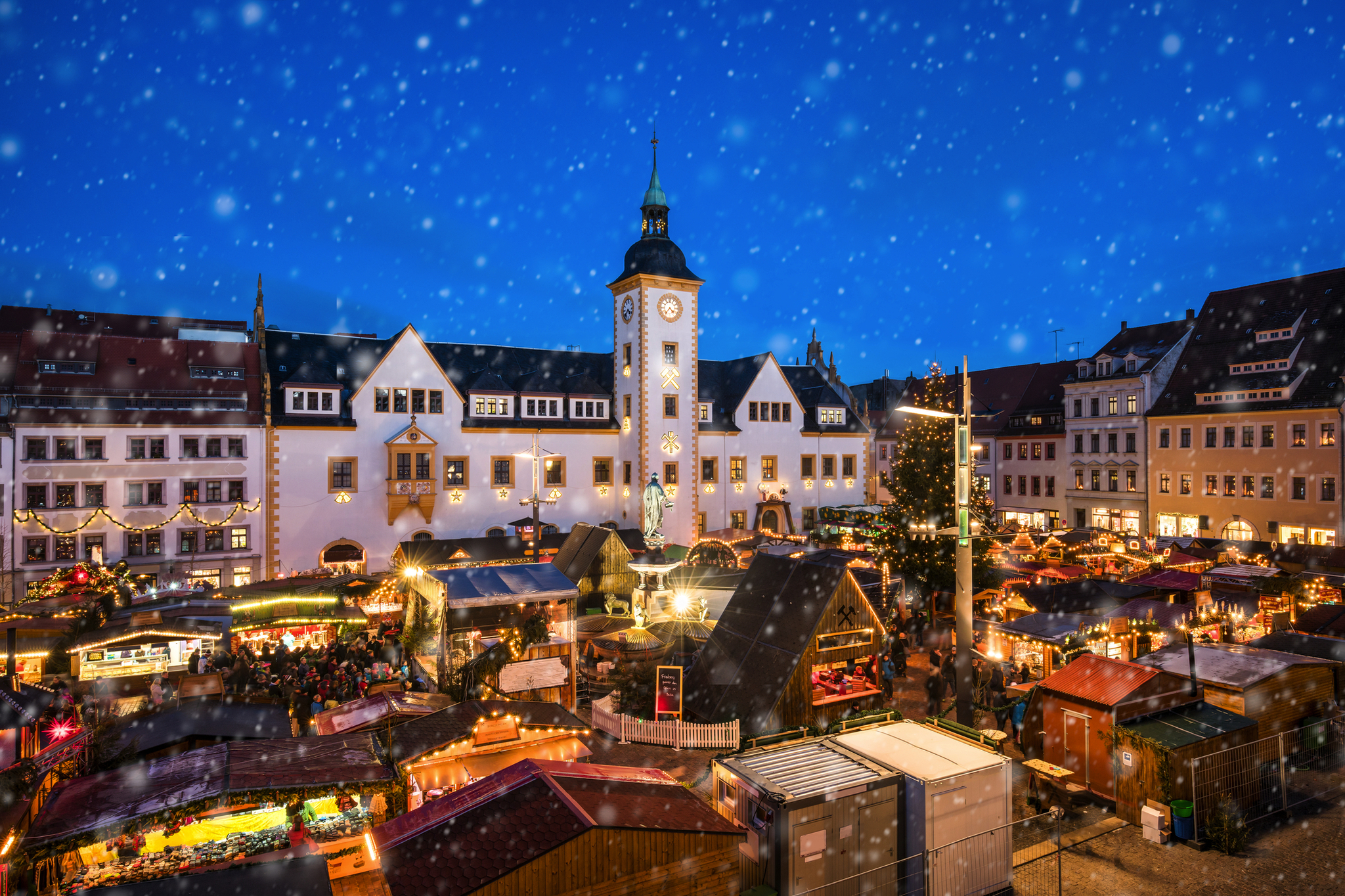 Weihnachtlicher Markt mit Lichtern und Schnee vor historischem Gebäude.