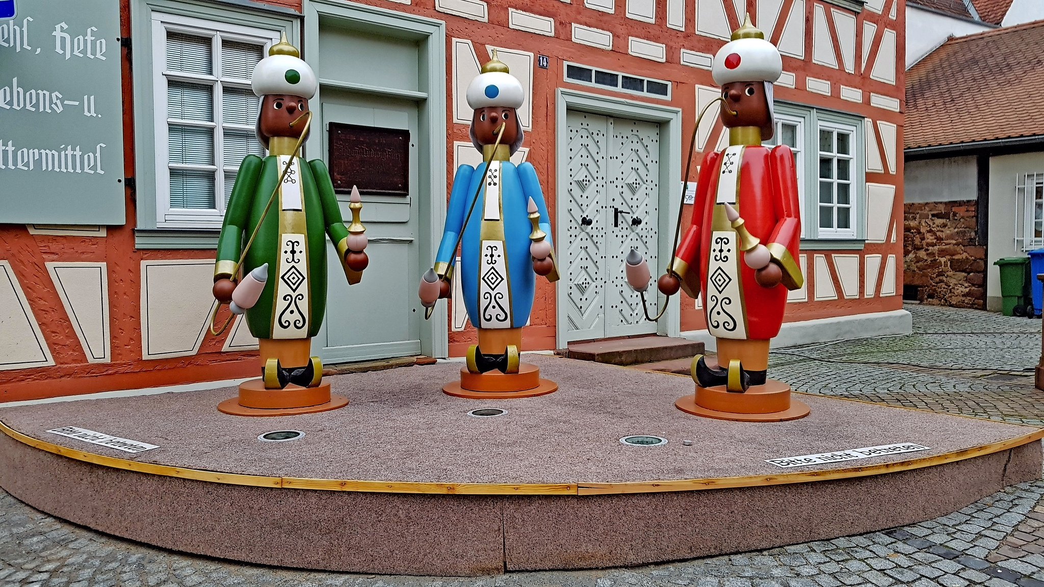 Drei lebensgroße Räuchermännchen vor einem Fachwerkhaus.