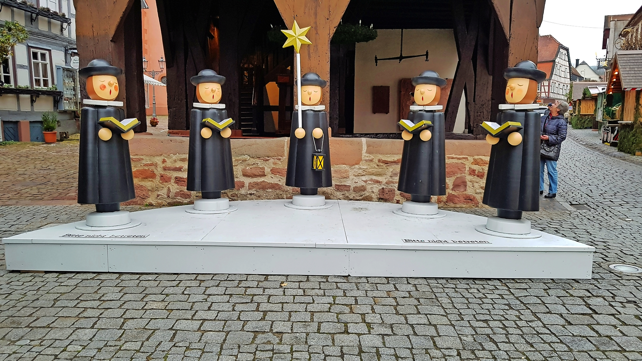 Holzfiguren von Kurrendesängern auf einem Marktplatz.