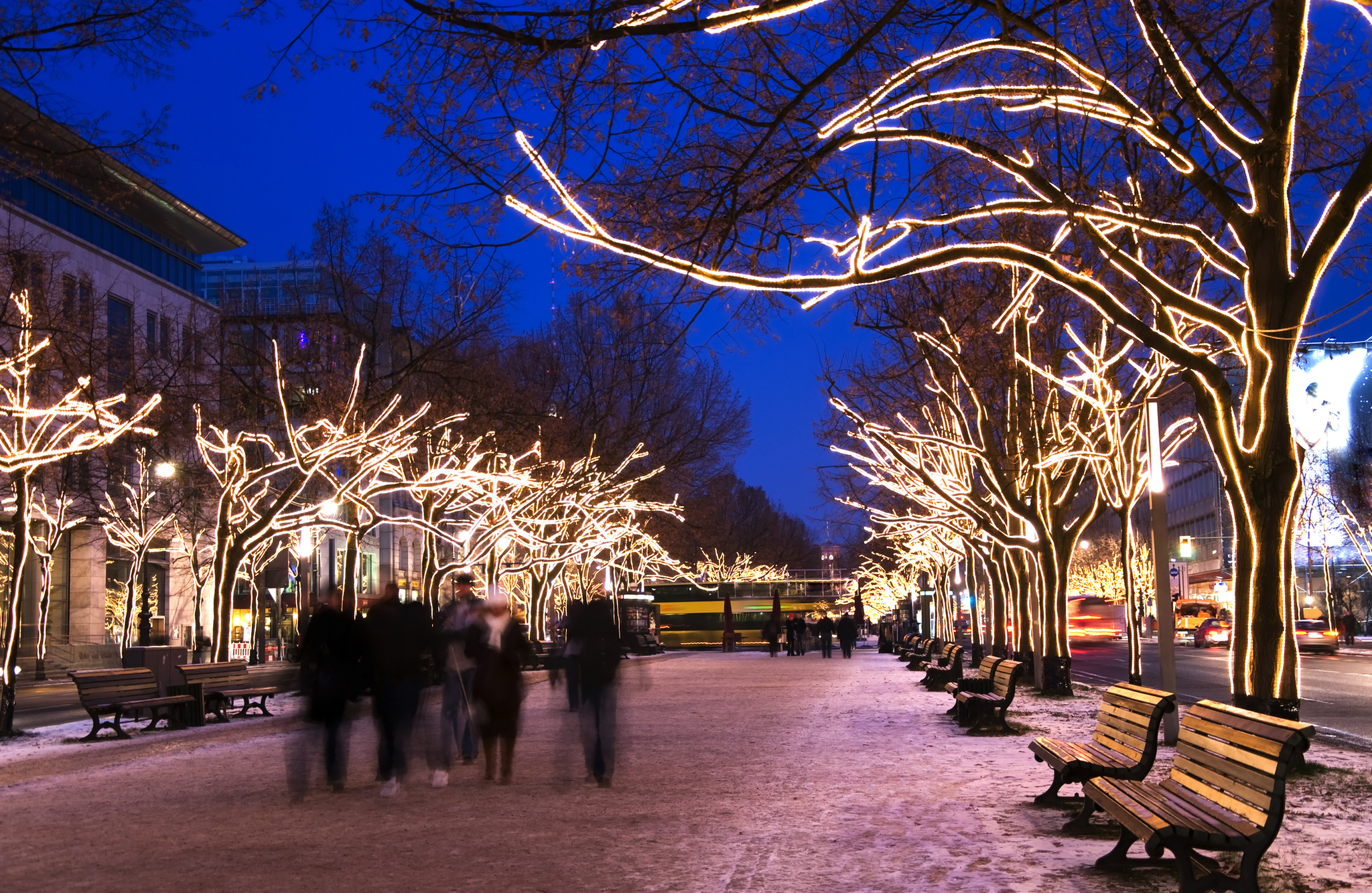 Beleuchtete Bäume und Menschen auf einem winterlichen Boulevard bei Abenddämmerung.
