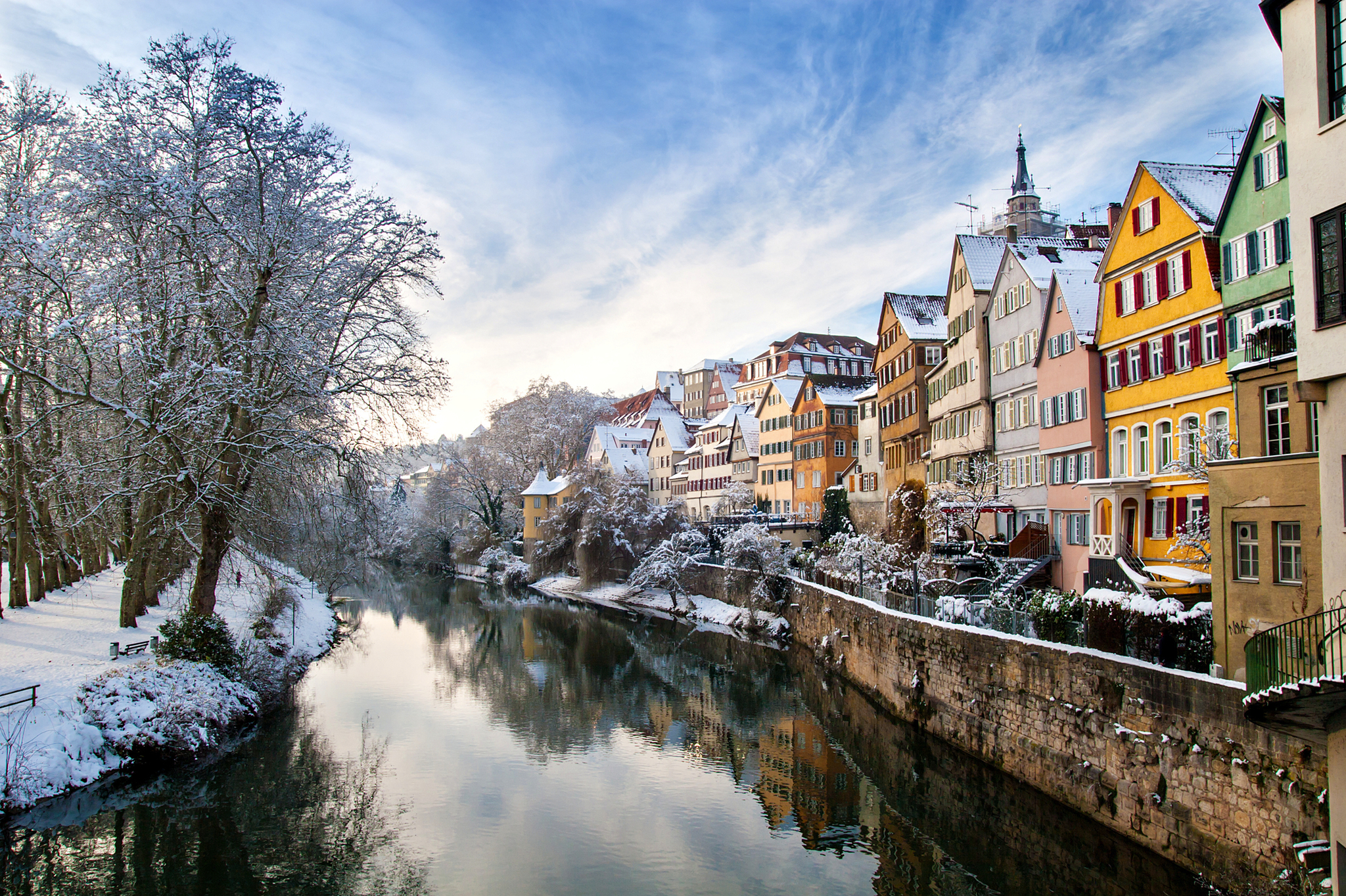 Verschneite Stadtansicht an einem Fluss mit bunten Häusern und Bäumen im Winter.
