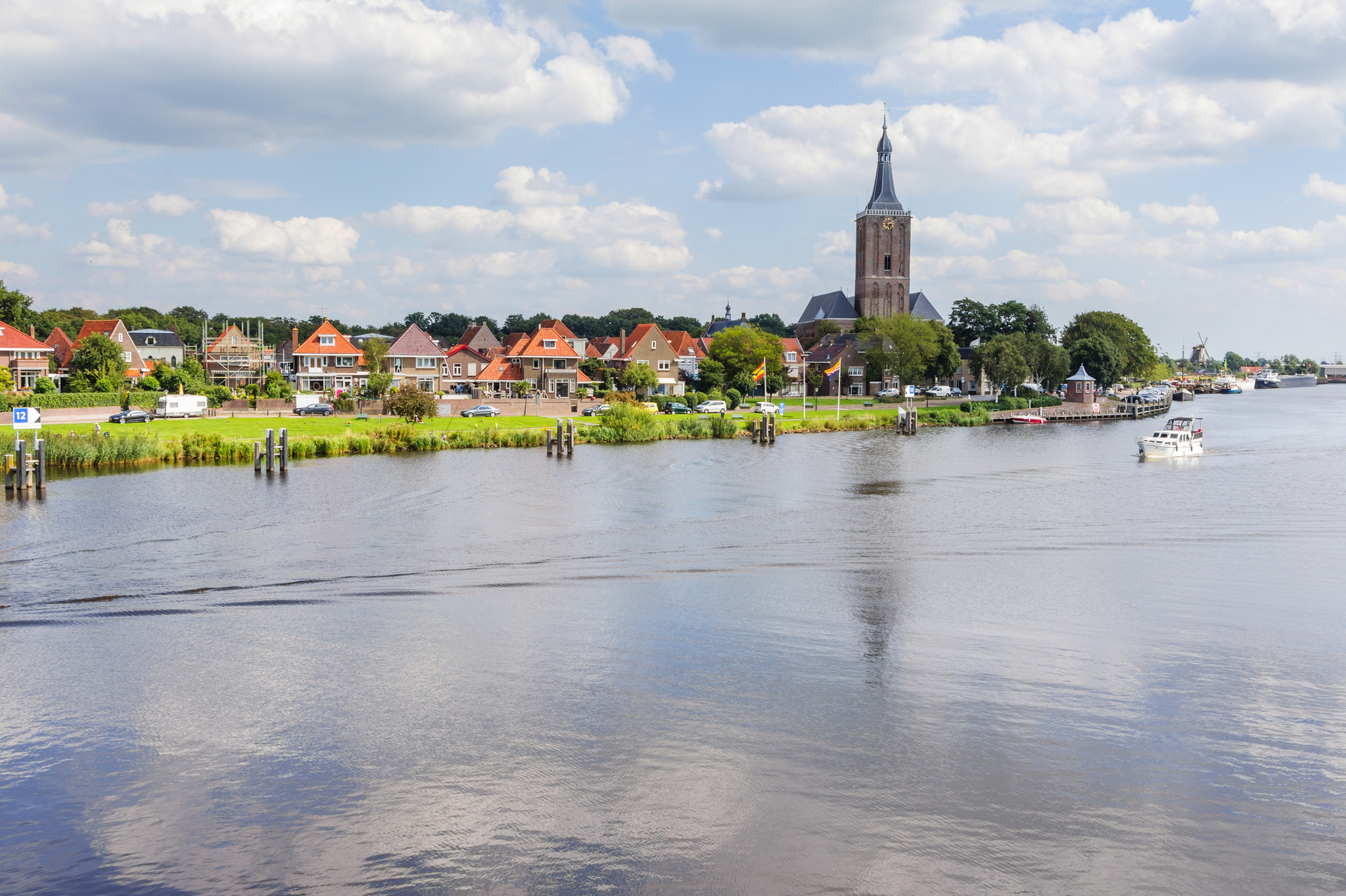 Flusslandschaft mit Kirche und Häusern im Hintergrund unter bewölktem Himmel.