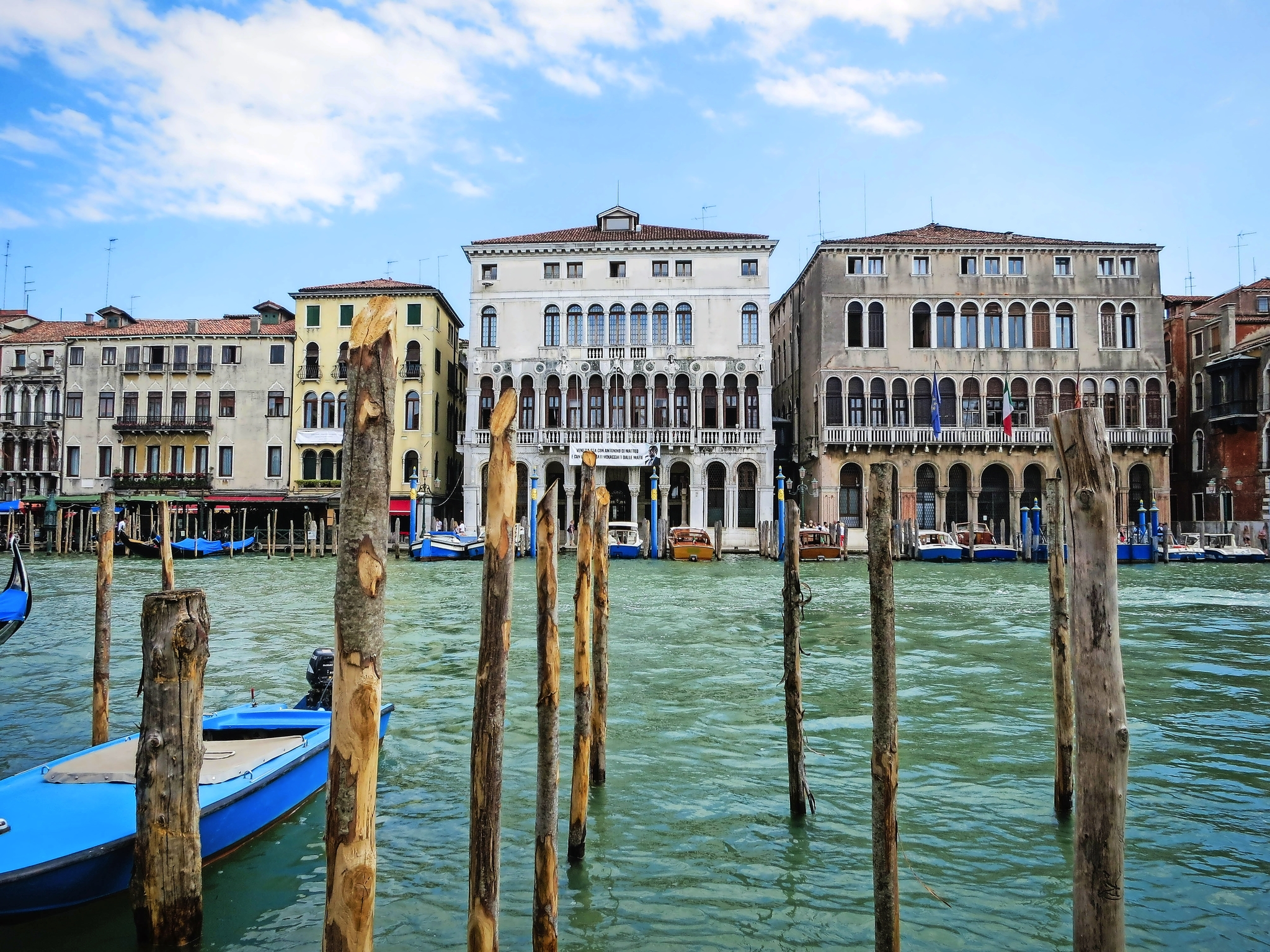 Venedig im Nordosten Italiens Gebäude am Kanal mit Booten und Wasserpfählen bei blauem Himmel.