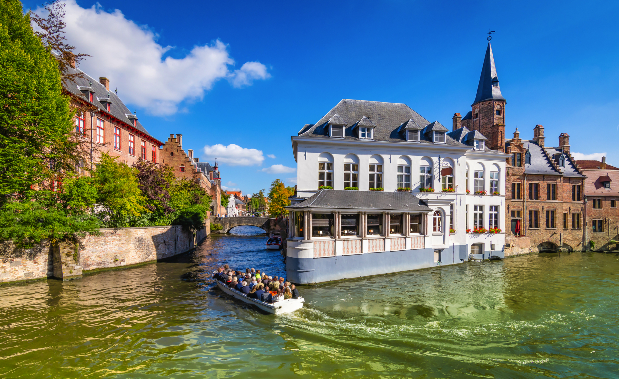Kanal in Brügge mit historischer Architektur und Touristenboot bei sonnigem Wetter