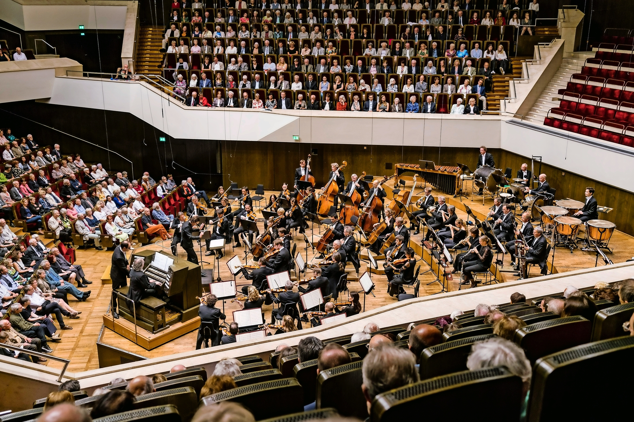 Orchester spielt in einem Konzertsaal, Publikum sitzt gespannt.