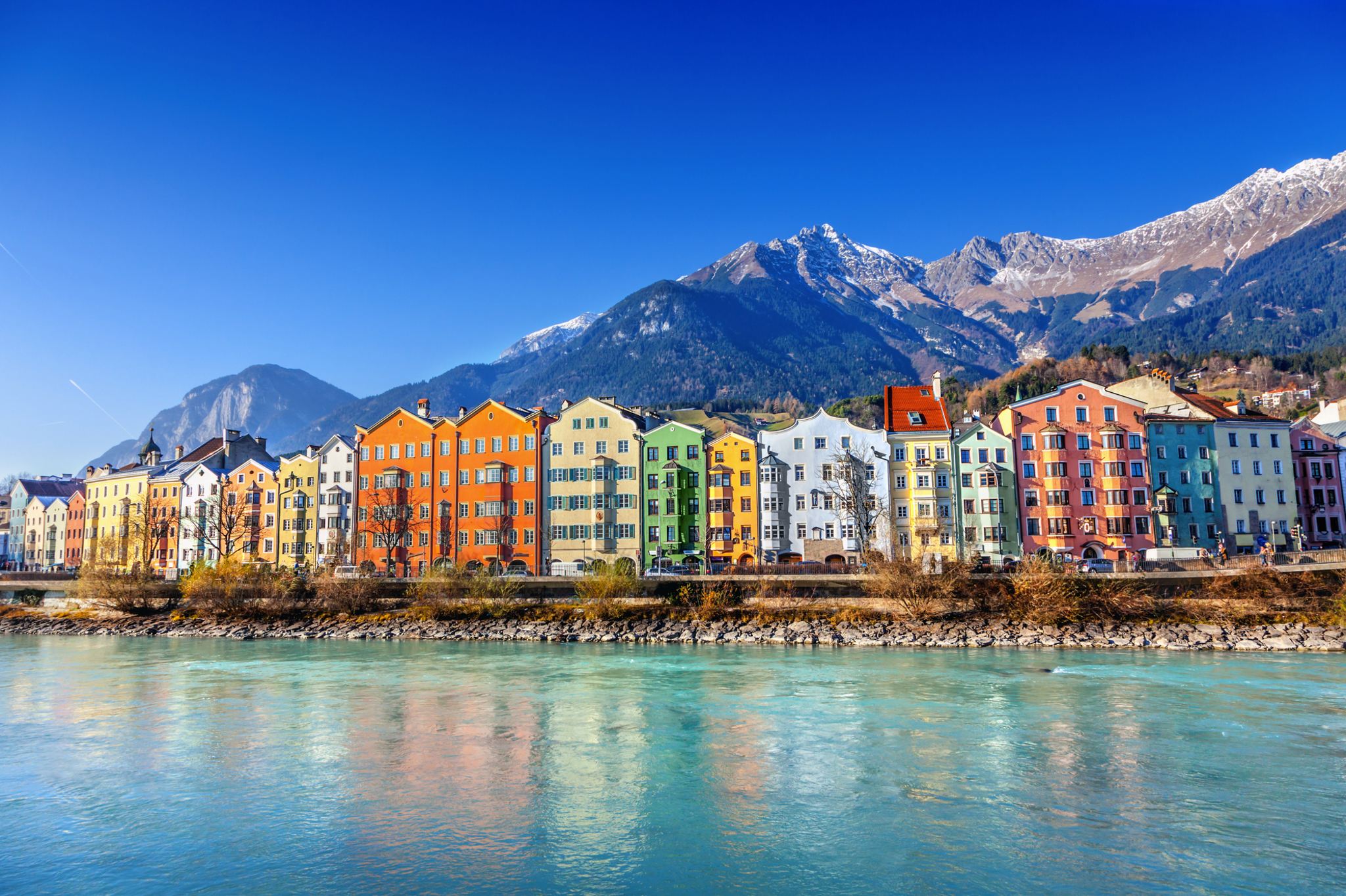 Bunte Gebäude am Flussufer mit Bergen im Hintergrund.