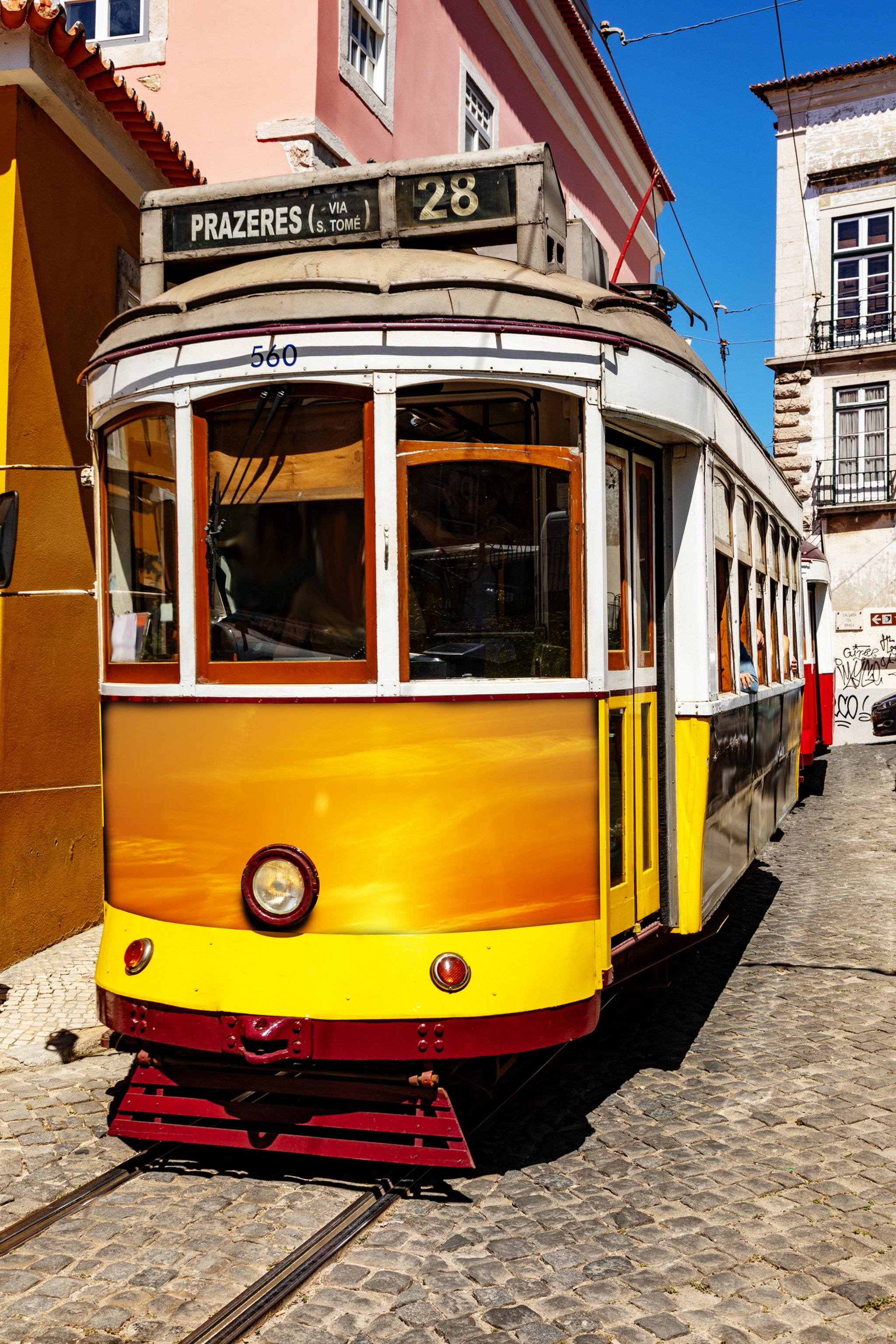 Gelbe Straßenbahn auf sonniger Kopfsteinpflasterstraße in Lissabon.