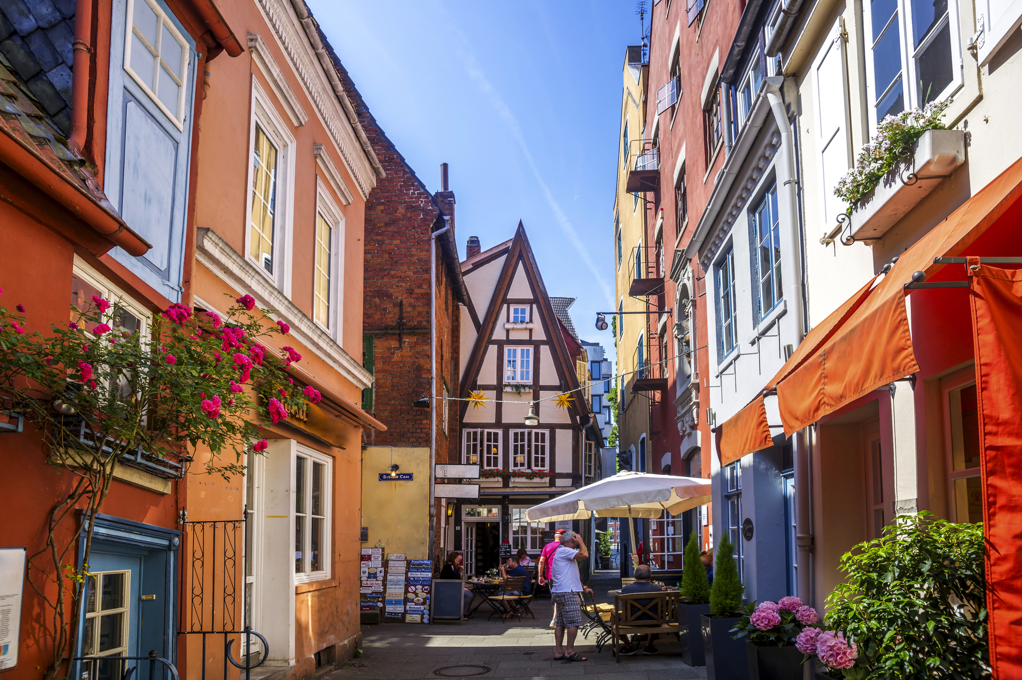 Enge Gasse mit Fachwerkhäusern und Straßencafé bei Sonnenschein.