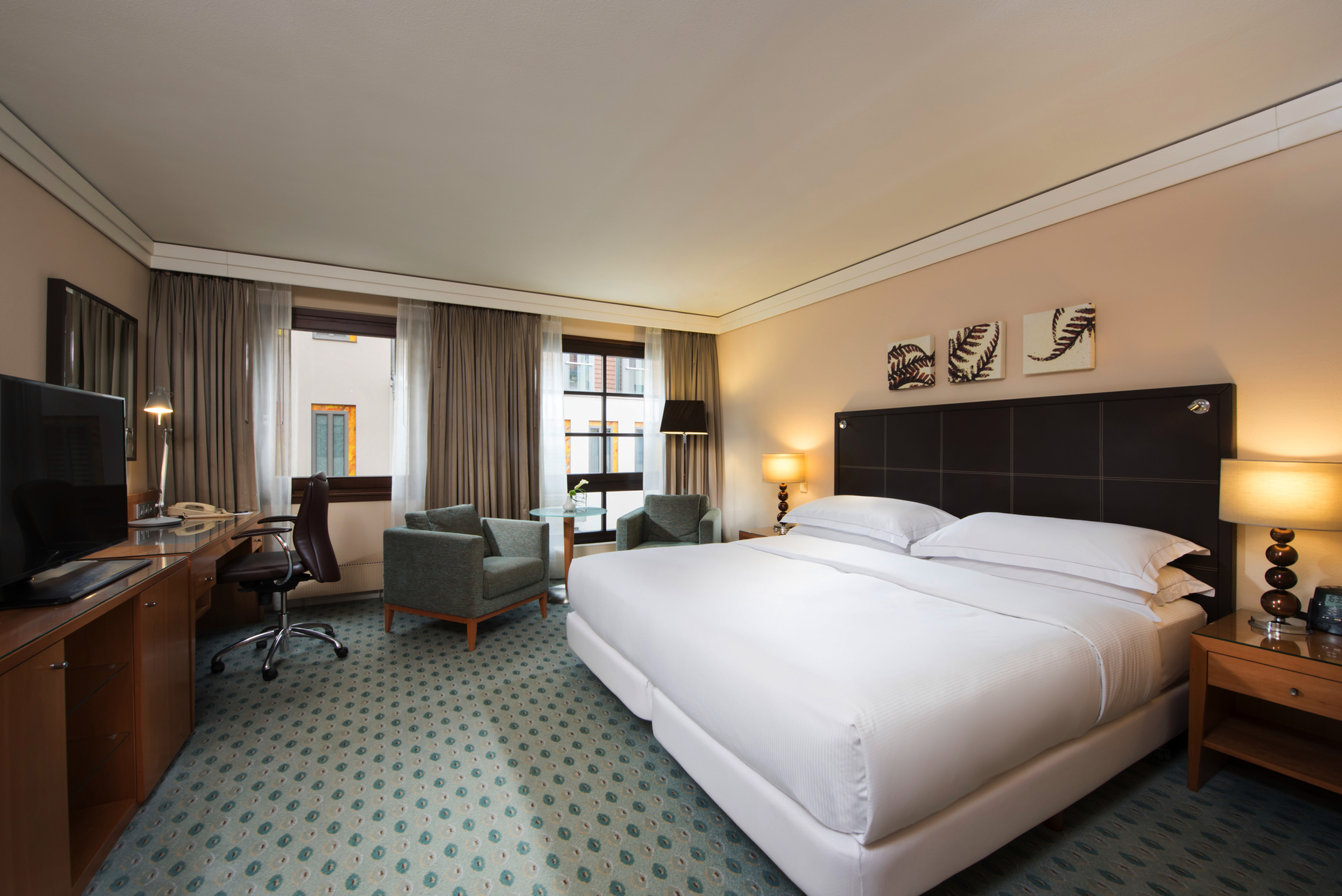 Doppelzimmer mit großem Bett, Schreibtisch, Sesseln und Fenster.