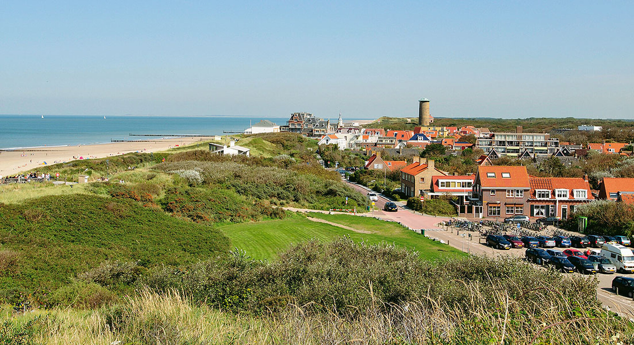 Küstenstadt Domburg mit Häusern, Strand, Dünen und Leuchtturm bei klarem Himmel.