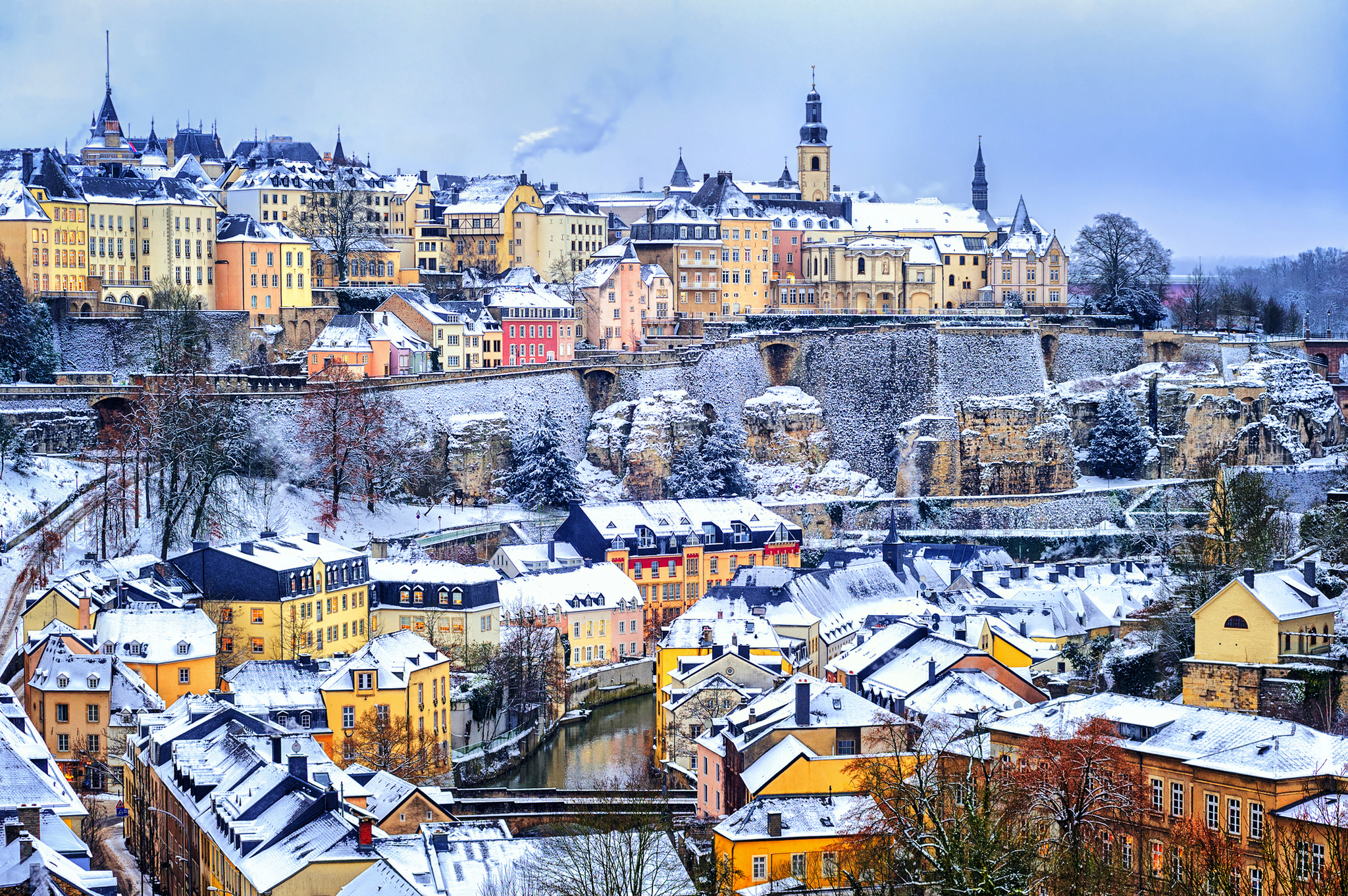 Verschneite Altstadt von Luxemburg mit historischen Gebäuden und Fluss im Vordergrund.