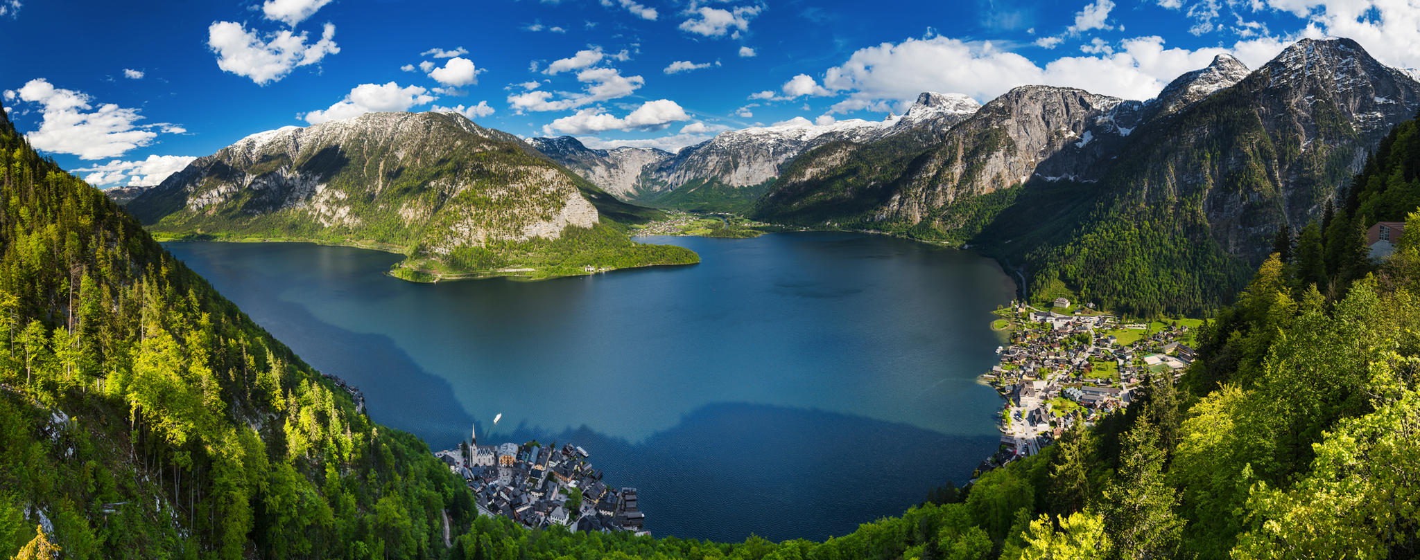 Panoramablick auf einen See inmitten von grünen Bergen und einem Dorf am Ufer.