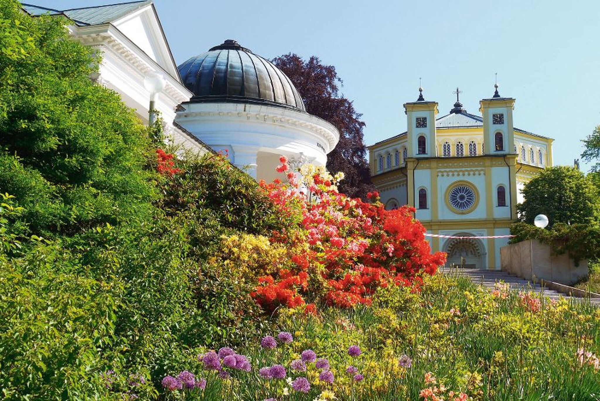 Gebäude mit Kuppel und orthodoxer Kirche, umgeben von blühenden Gärten in Marienbad, Tschechien.