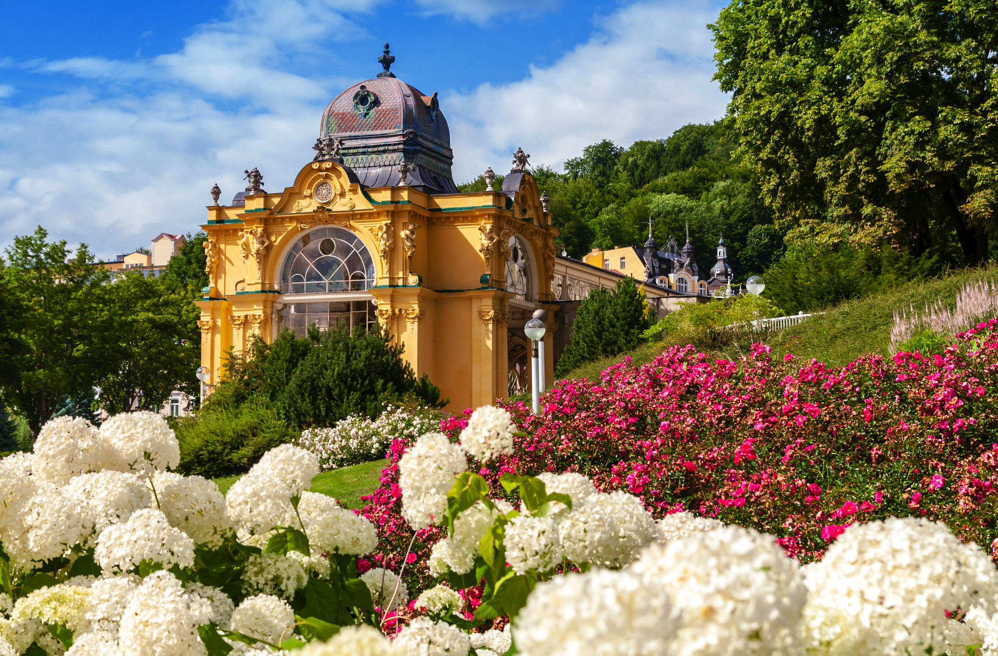 Historisches Gebäude mit Kuppeldach, umgeben von blühenden Gärten und Grün.
