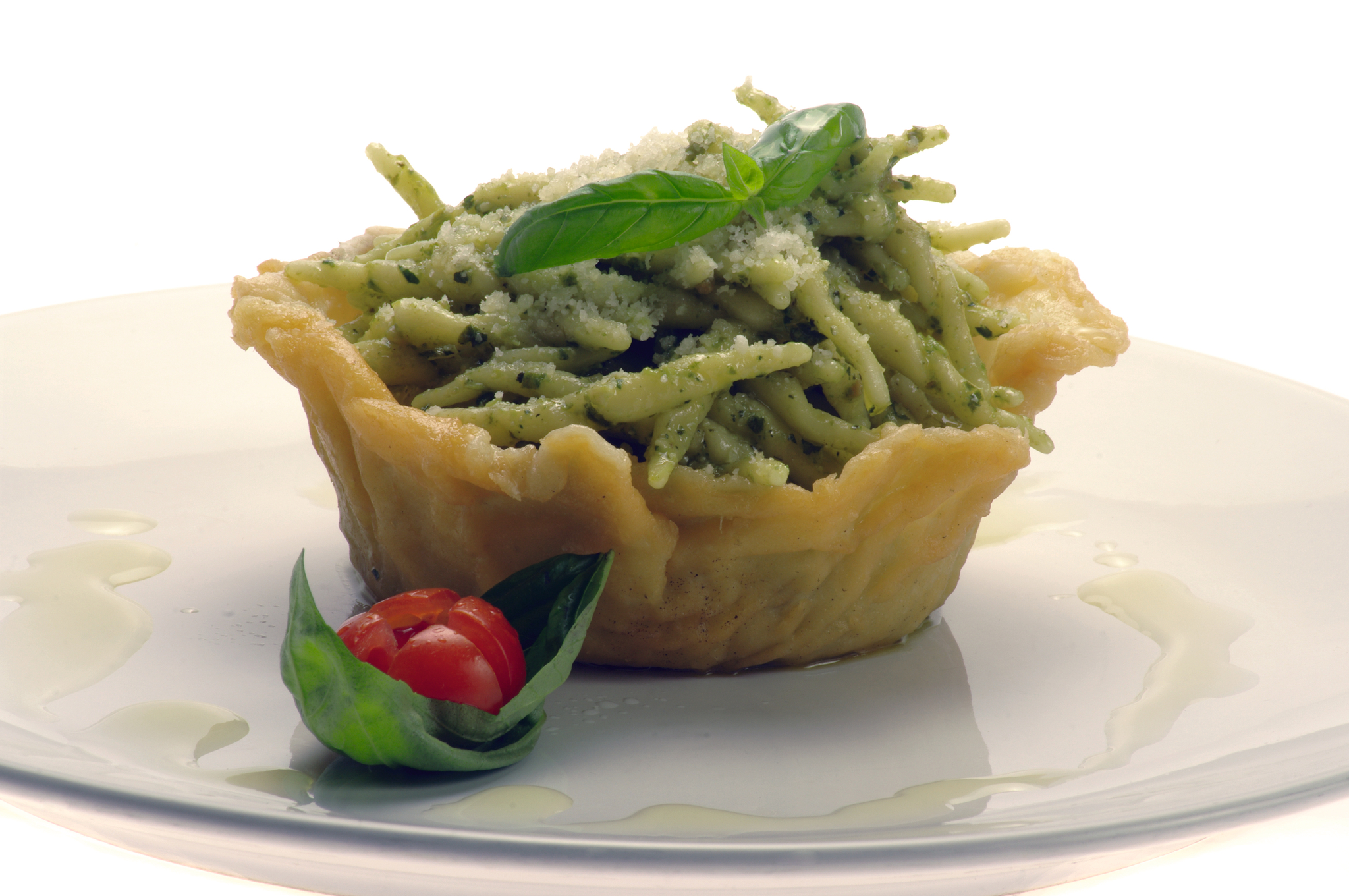 Tartalette mit Spaghetti und Pesto, dekoriert mit Basilikum und Kirschtomate.