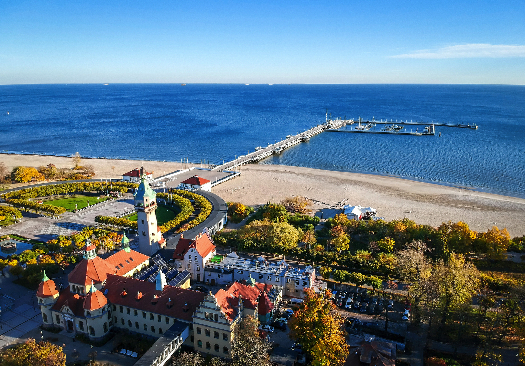 Luftaufnahme eines Strandes mit Hafenpier und Bäumen im Herbst.