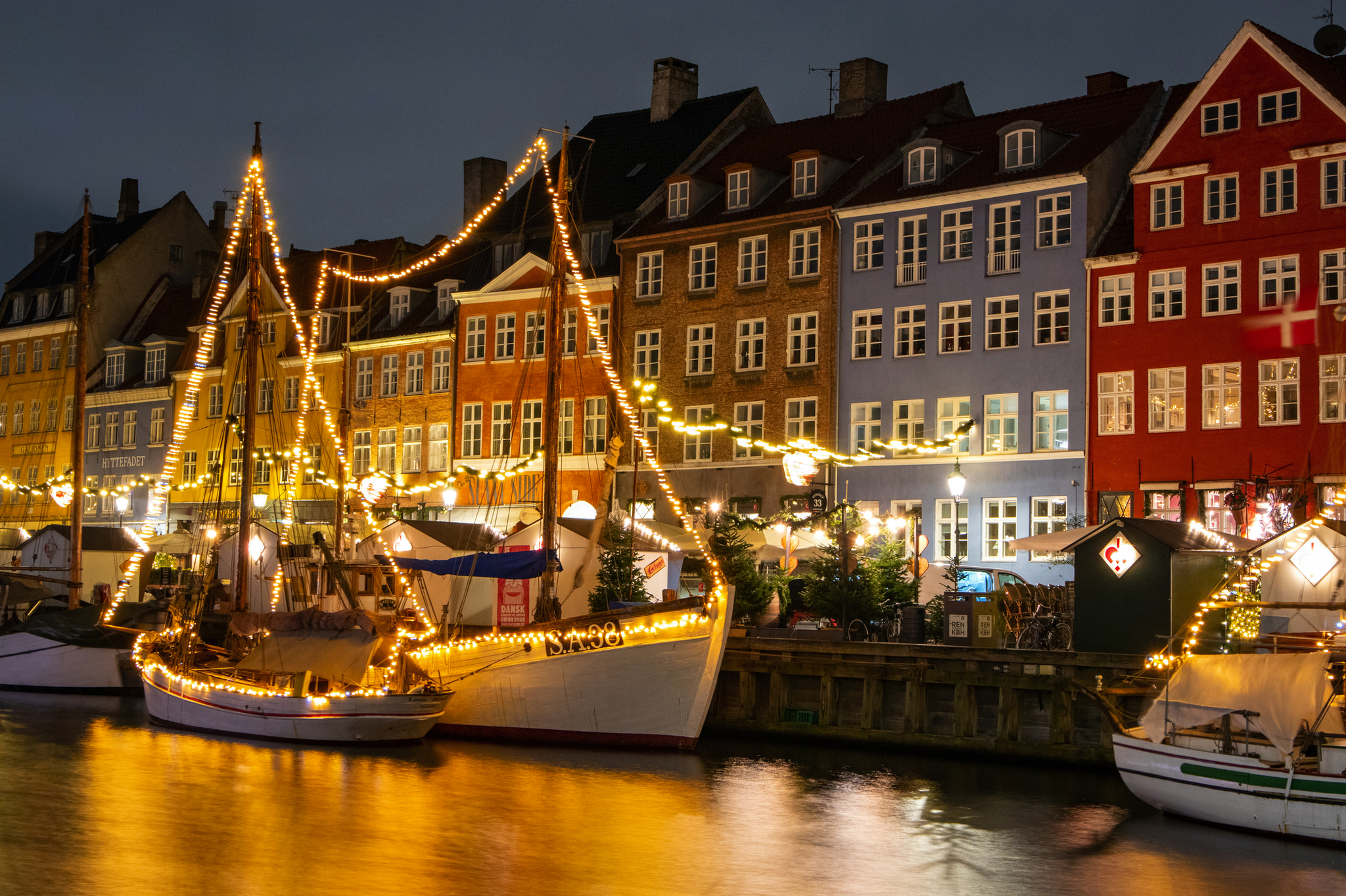 Lichtergeschmückte Boote und bunte Häuser an einem Kanal bei Nacht.
