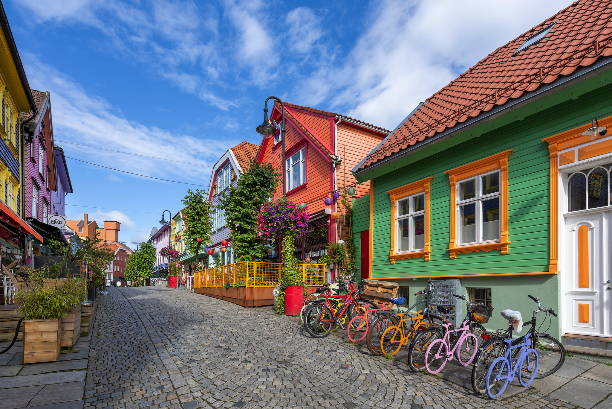 Bunte Häuserzeile mit Fahrrädern in kopfsteingepflasterter Straße bei blauem Himmel.
