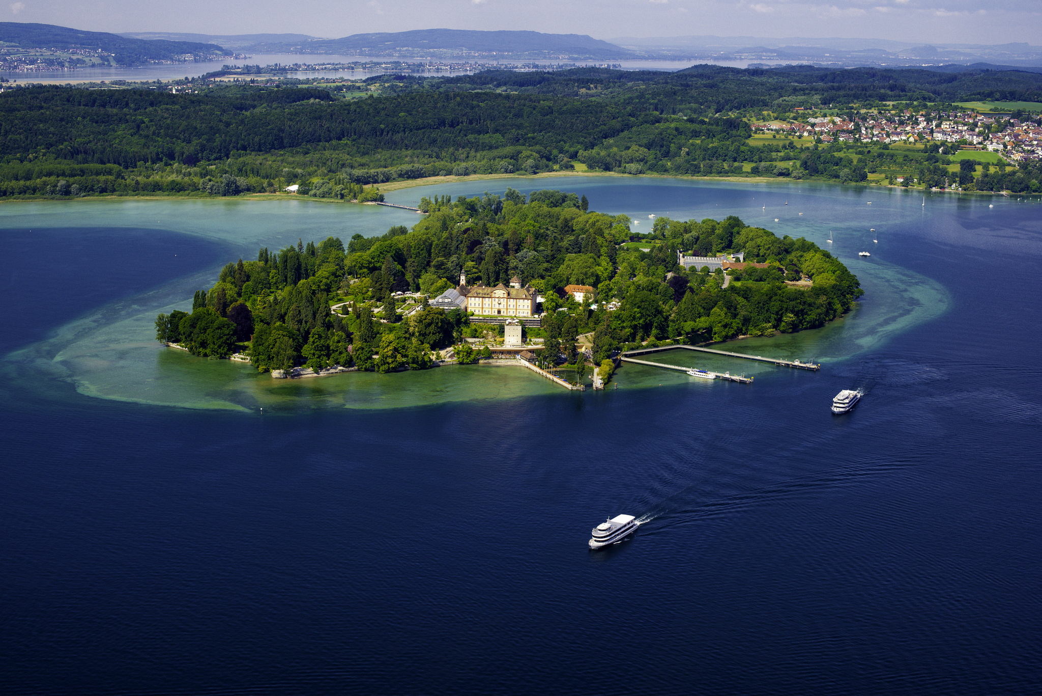 Luftaufnahme der Insel Mainau im Bodensee, umgeben von blauem Wasser und bewaldeter Landschaft.