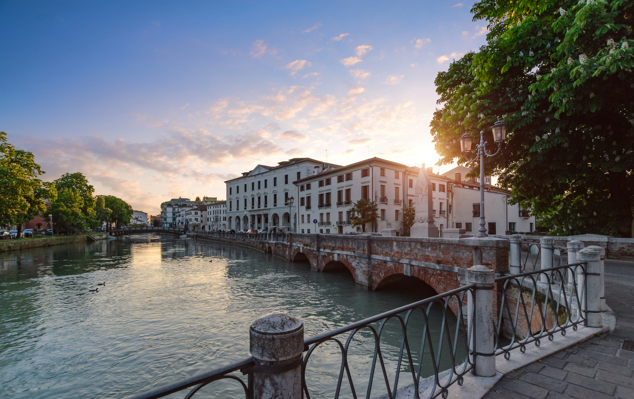 Flussbrücke bei Sonnenuntergang mit historischen Gebäuden und Bäumen im Hintergrund