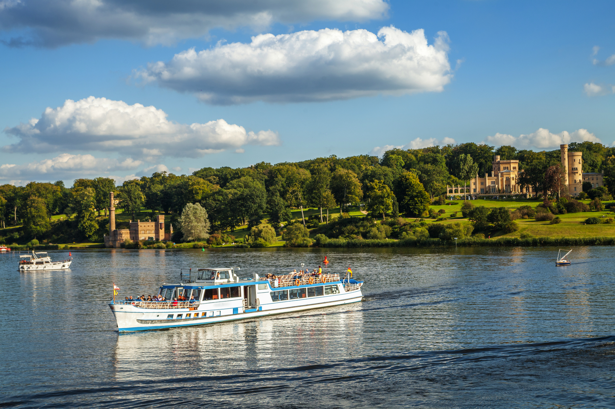 Ausflugsboot auf einem Fluss vor einer malerischen Landschaft mit Schloss im Hintergrund.